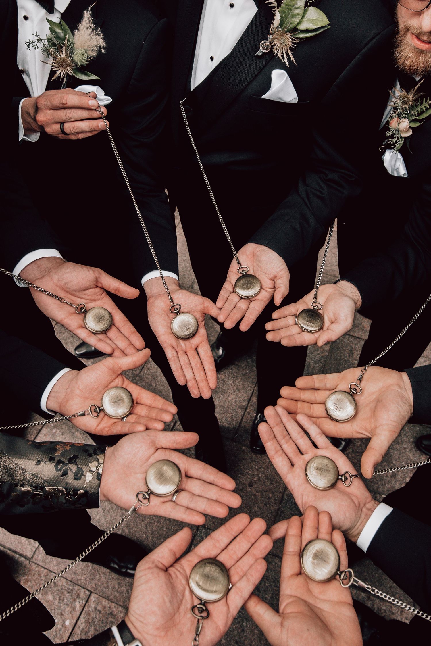 Groomsmen in black tuxedos display matching vintage pocket watches on chains in circular arrangement.