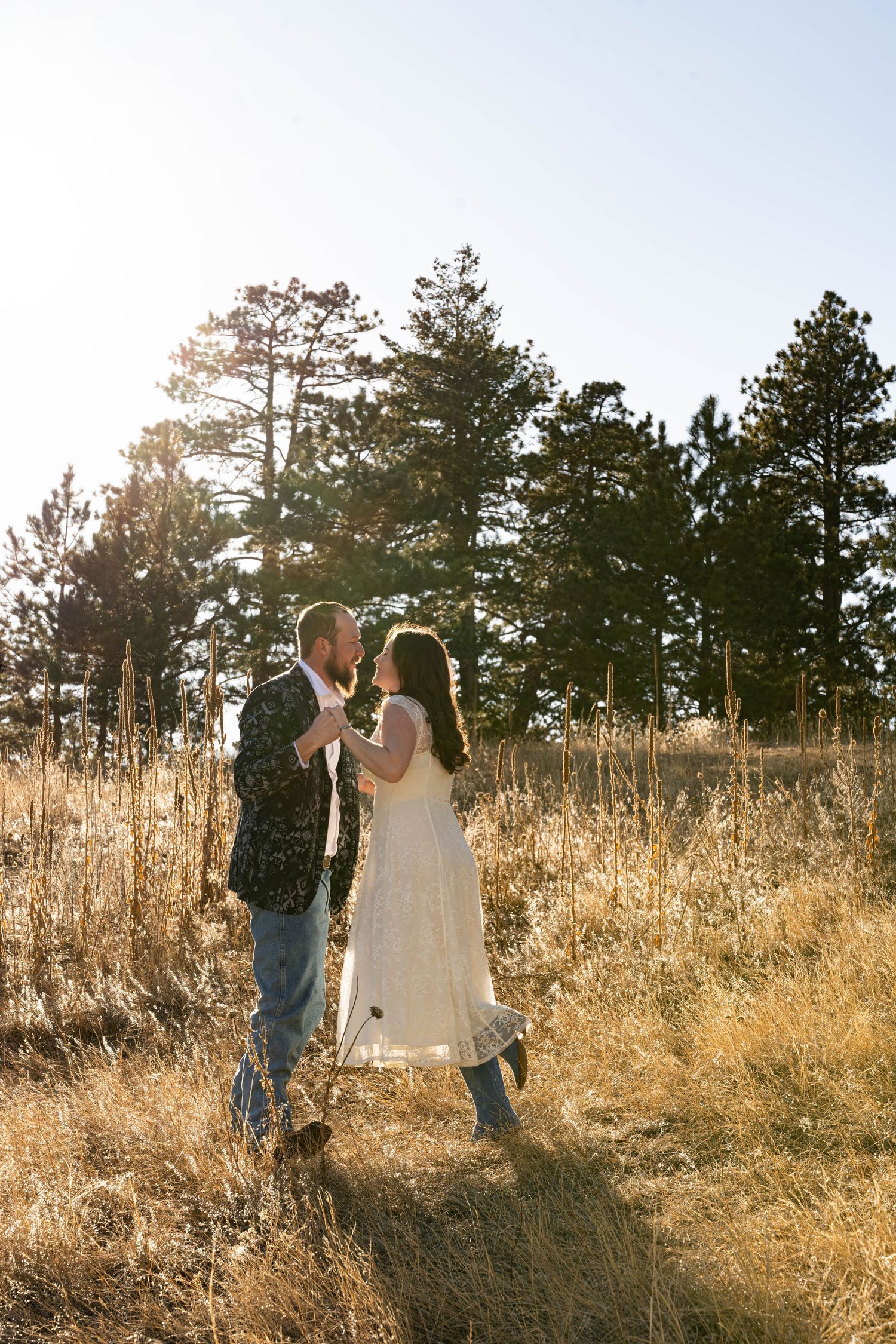 Couple sharing a romantic moment in a golden field with pine trees and bright backlight.