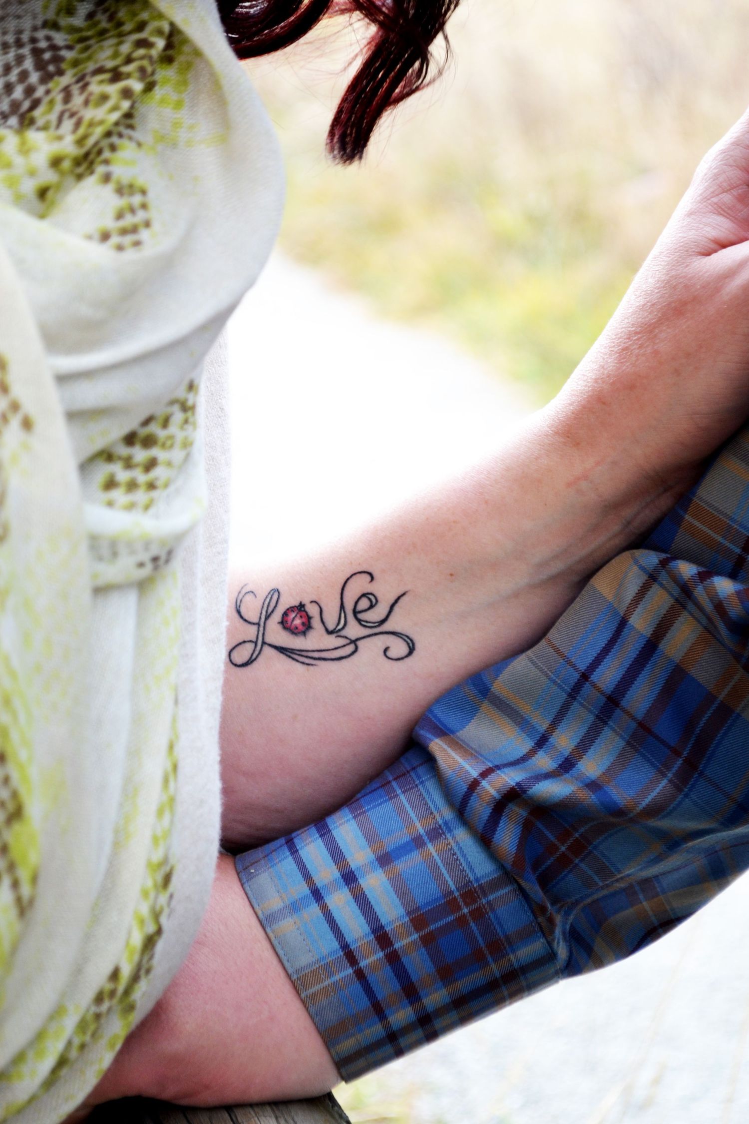 Close-up of a decorative Love tattoo with a pink flower accent on a womans wrist or ankle.