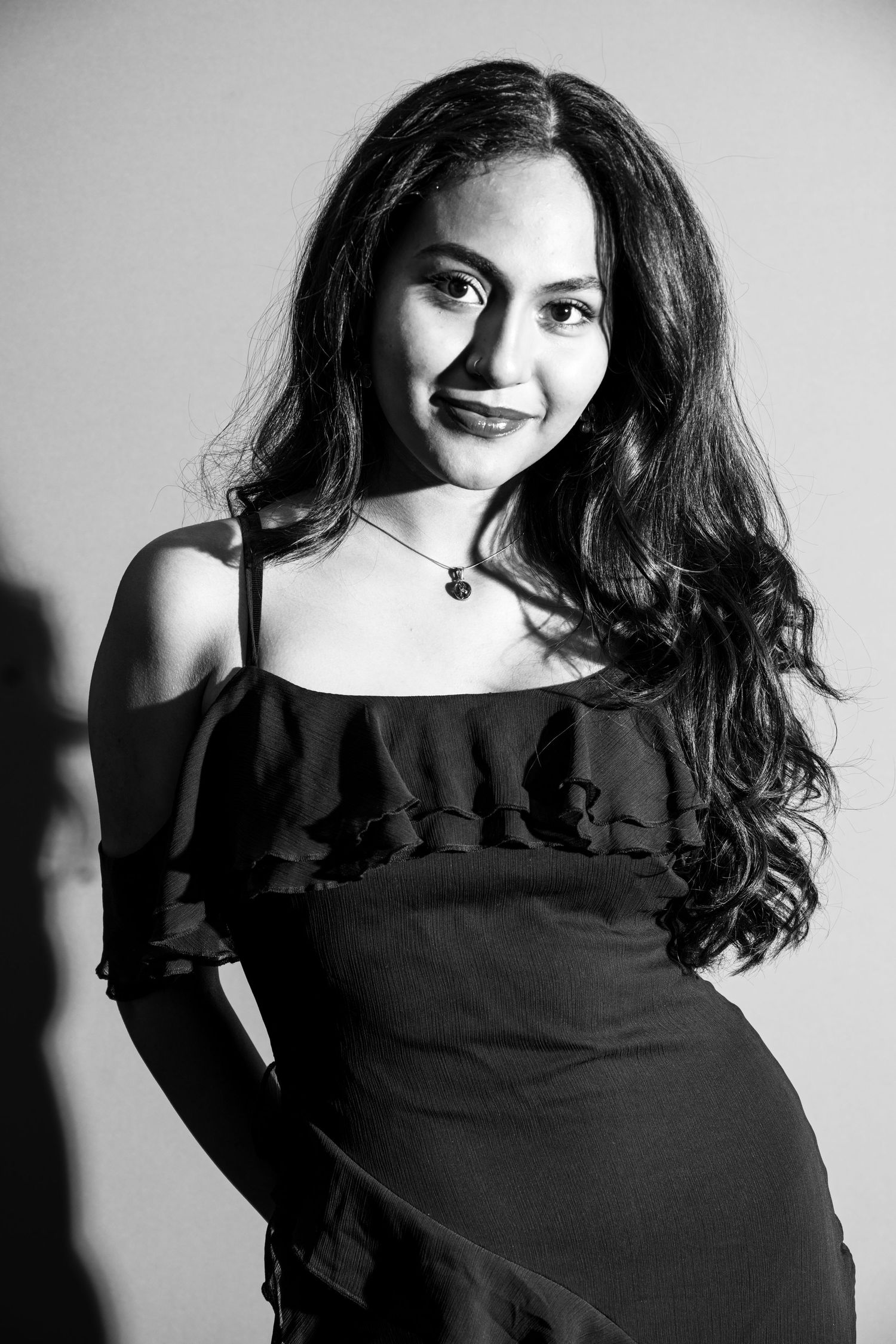 Black and white portrait of young woman in off-shoulder ruffled dress with wavy hair.