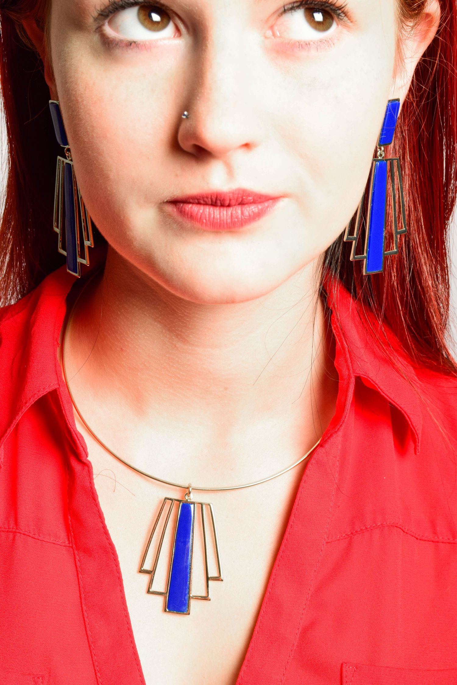 Woman wearing blue and gold geometric Art Deco necklace and matching earrings with red shirt.