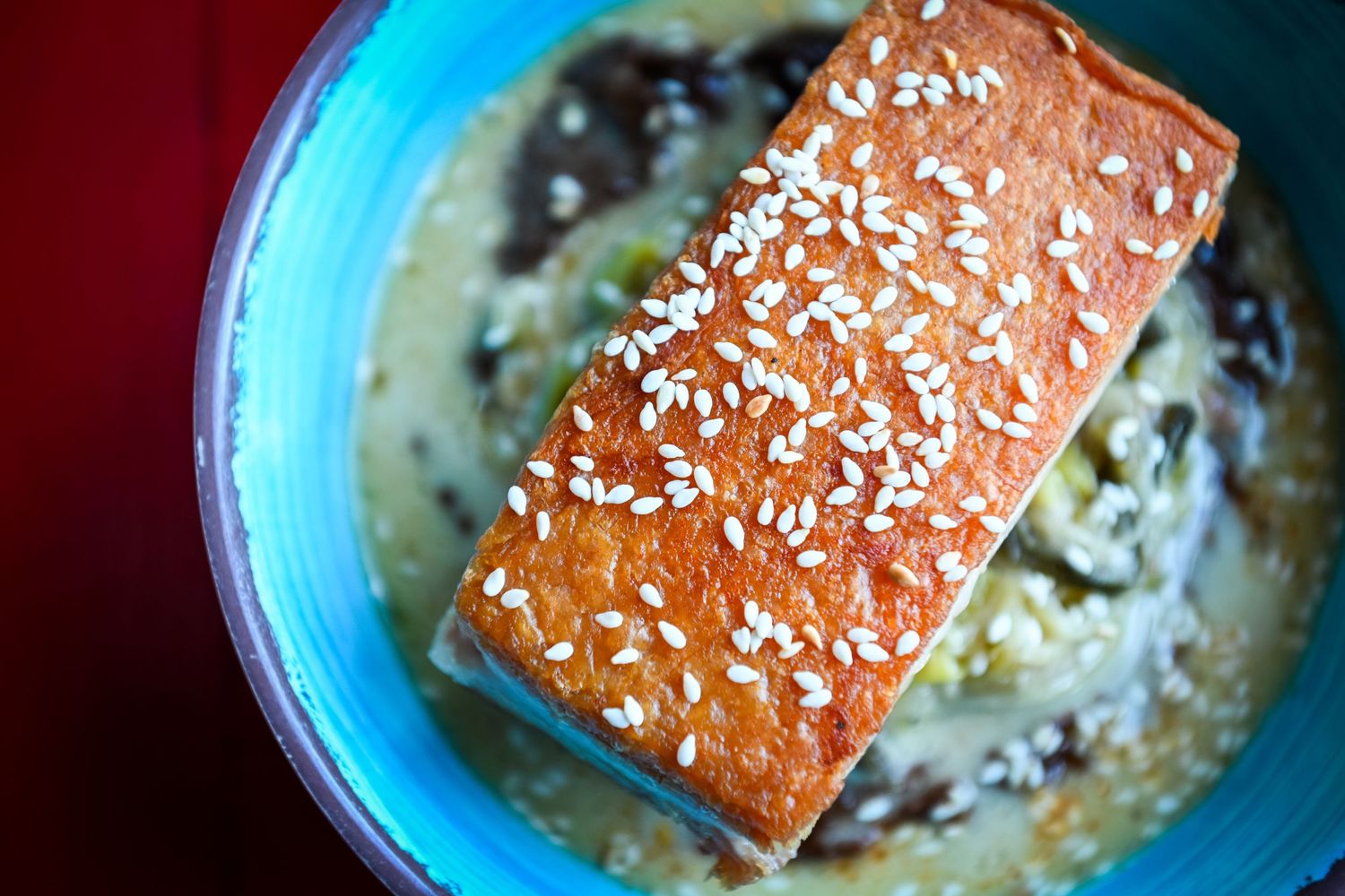 Crispy sesame-crusted salmon fillet served in a blue bowl with creamy mushroom sauce.