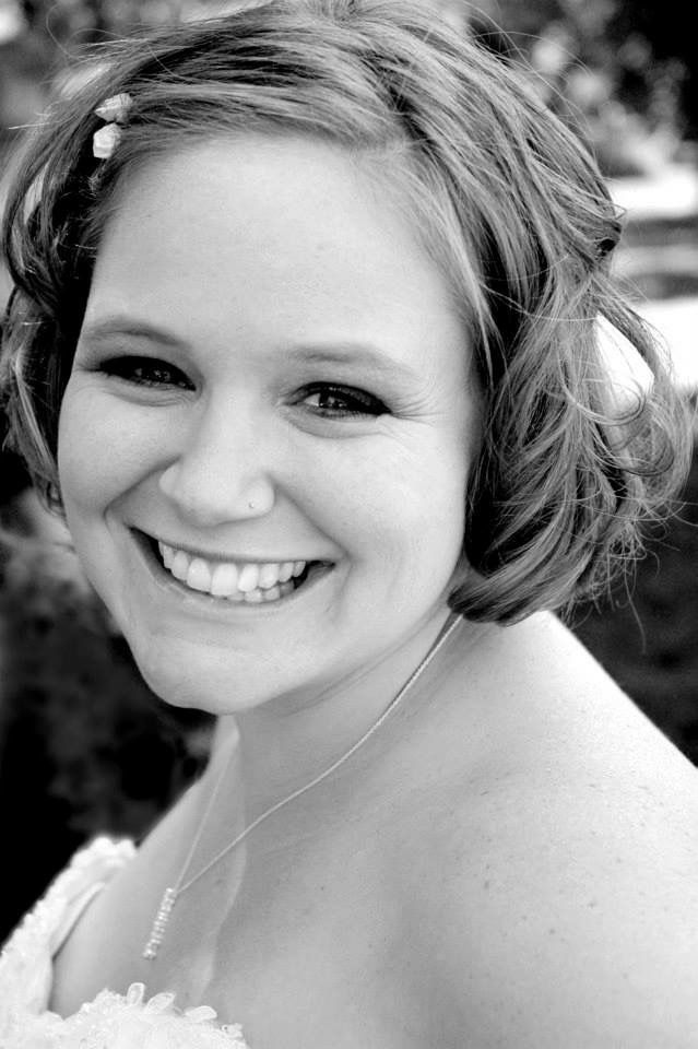 Black and white close-up portrait of a smiling bride with short hair and floral hair accessory on her wedding day.