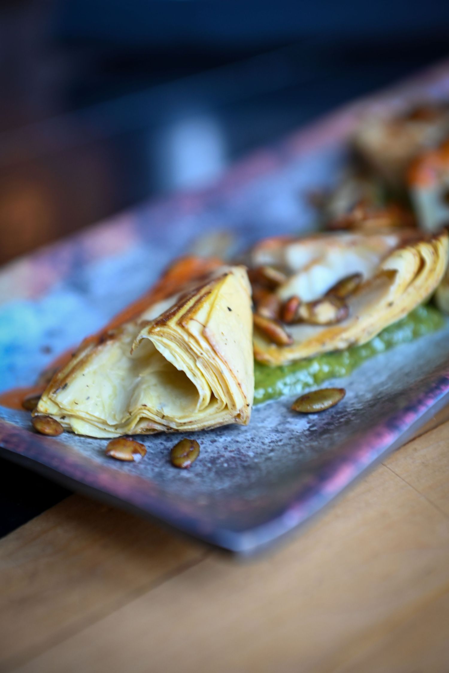 Savory crepes folded on a rustic blue plate with green sauce and toasted pumpkin seeds.