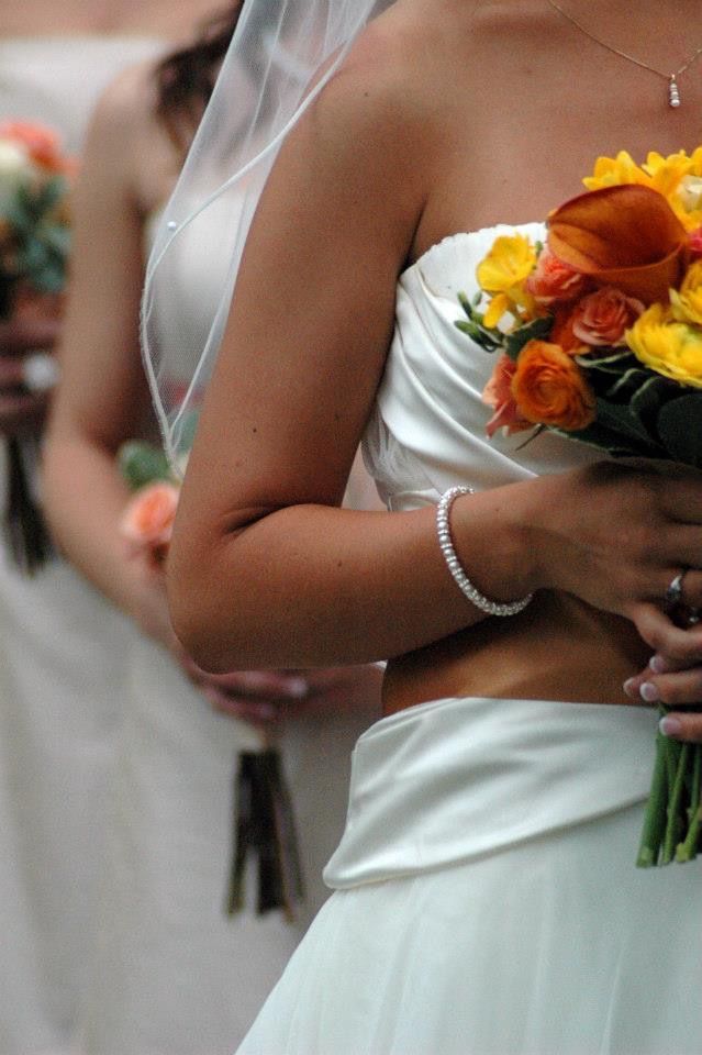 Bride in white strapless gown holding a vibrant bouquet of orange and yellow roses and calla lilies.