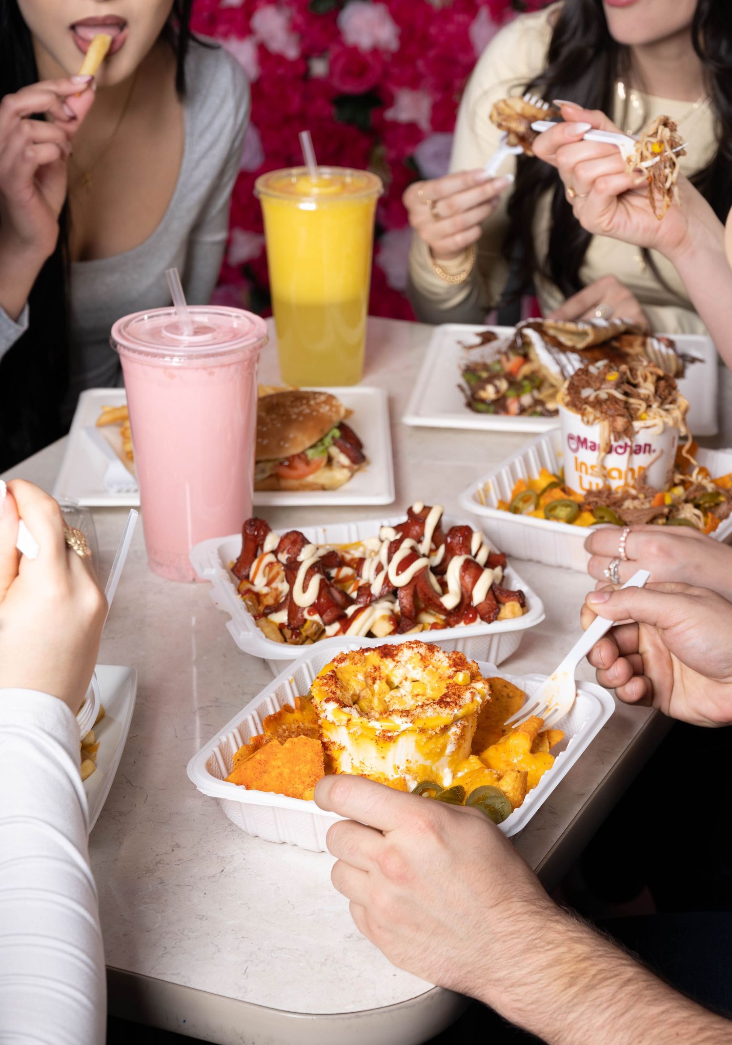 Group of friends sharing burgers, fries, and colorful drinks at an outdoor food table.