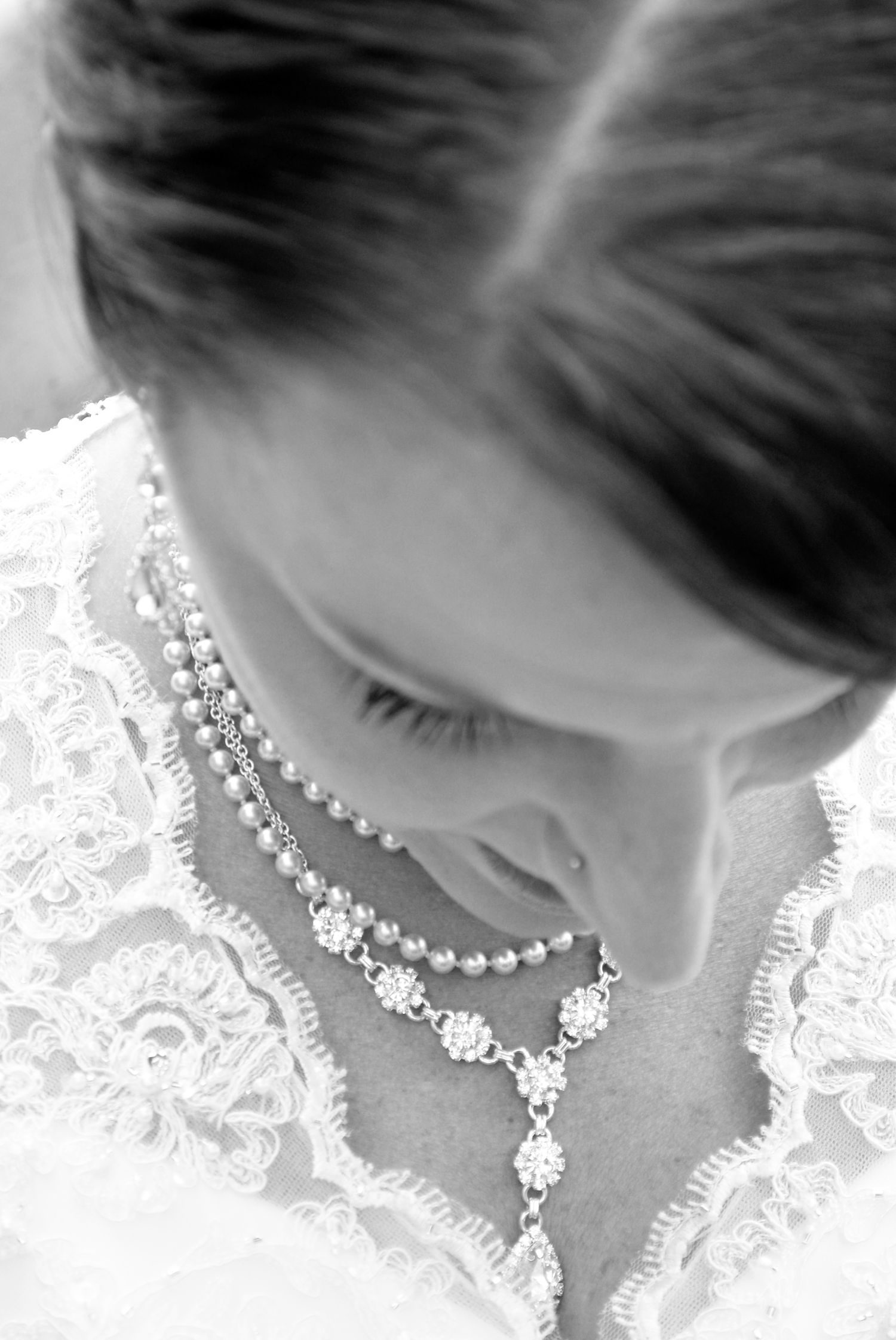 Black and white close-up of a bride wearing a pearl and crystal necklace over a lace wedding gown.