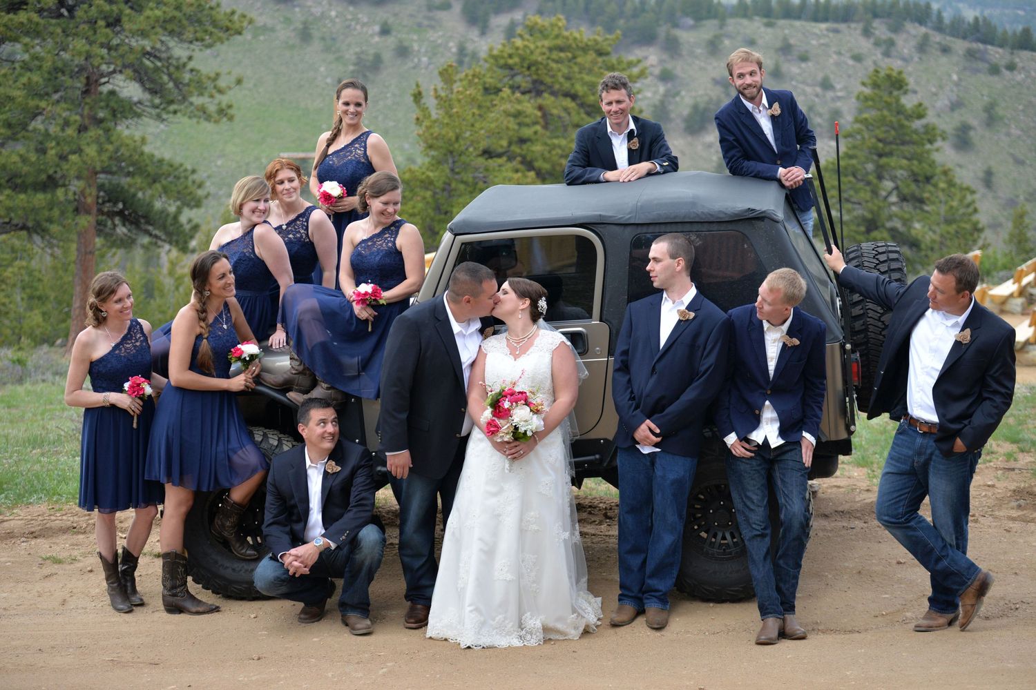 Wedding party in navy blue poses around a vintage Jeep at a rustic outdoor mountain location.