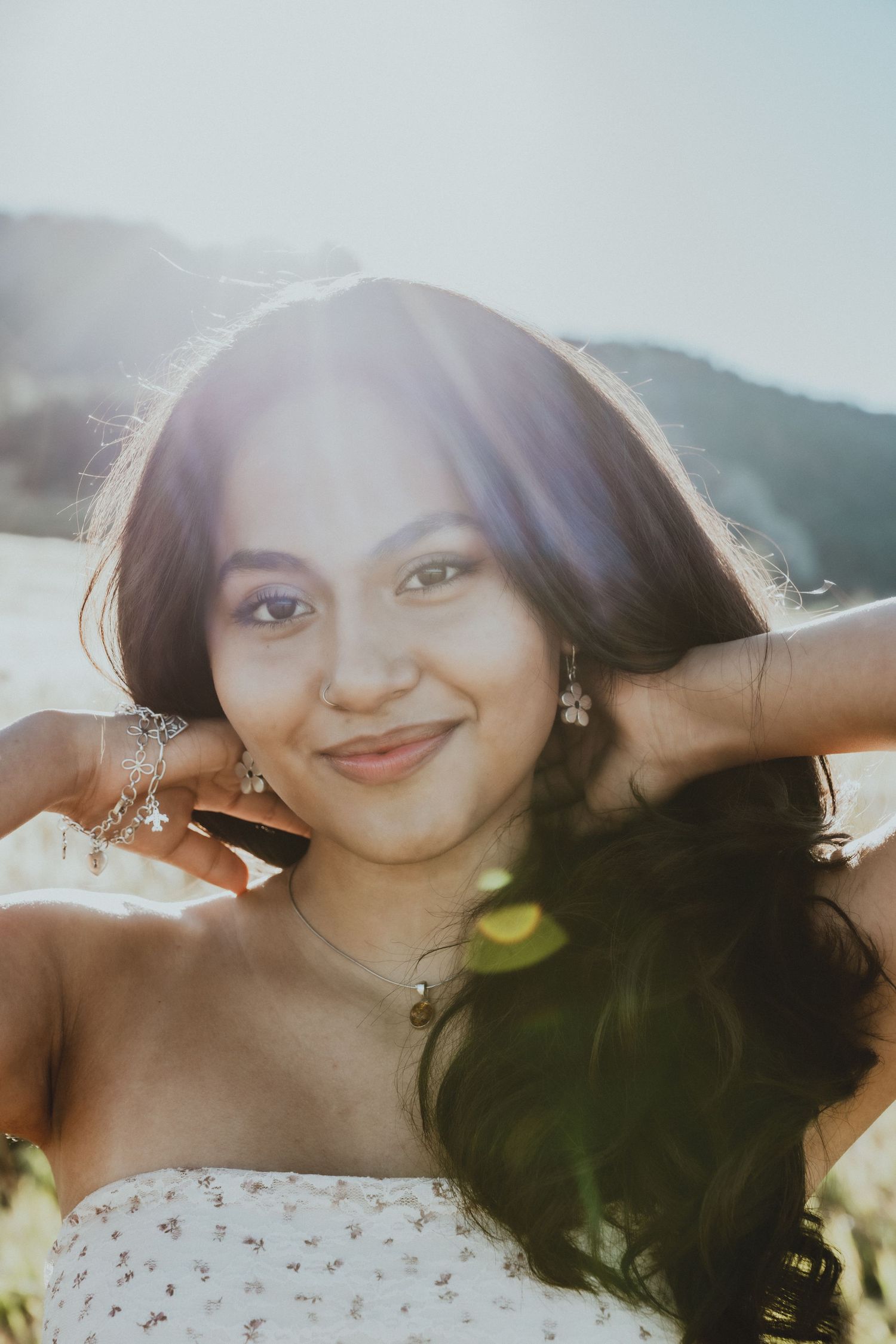 Smiling young woman with long dark hair in sunlit outdoor portrait with lens flare.