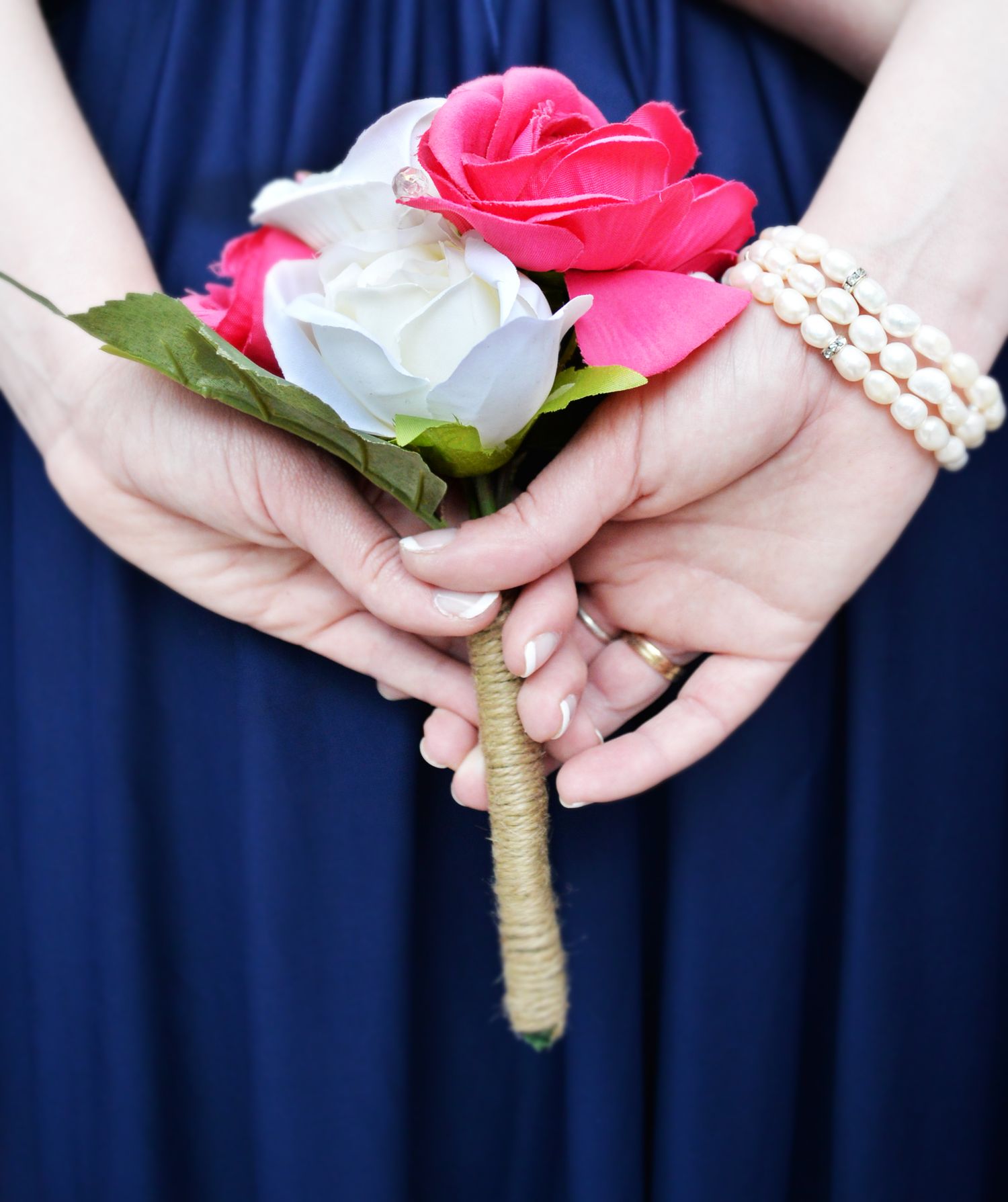 Bridesmaid in navy blue dress holding a small bouquet of pink and white roses with a pearl bracelet.