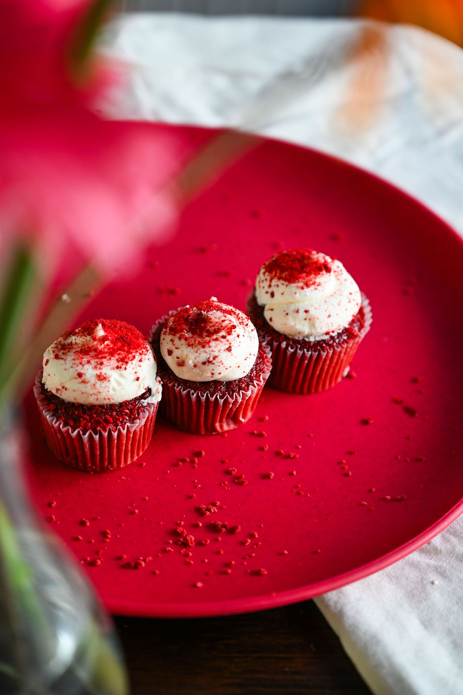 Three red velvet cupcakes with cream cheese frosting on a heart-shaped red plate.