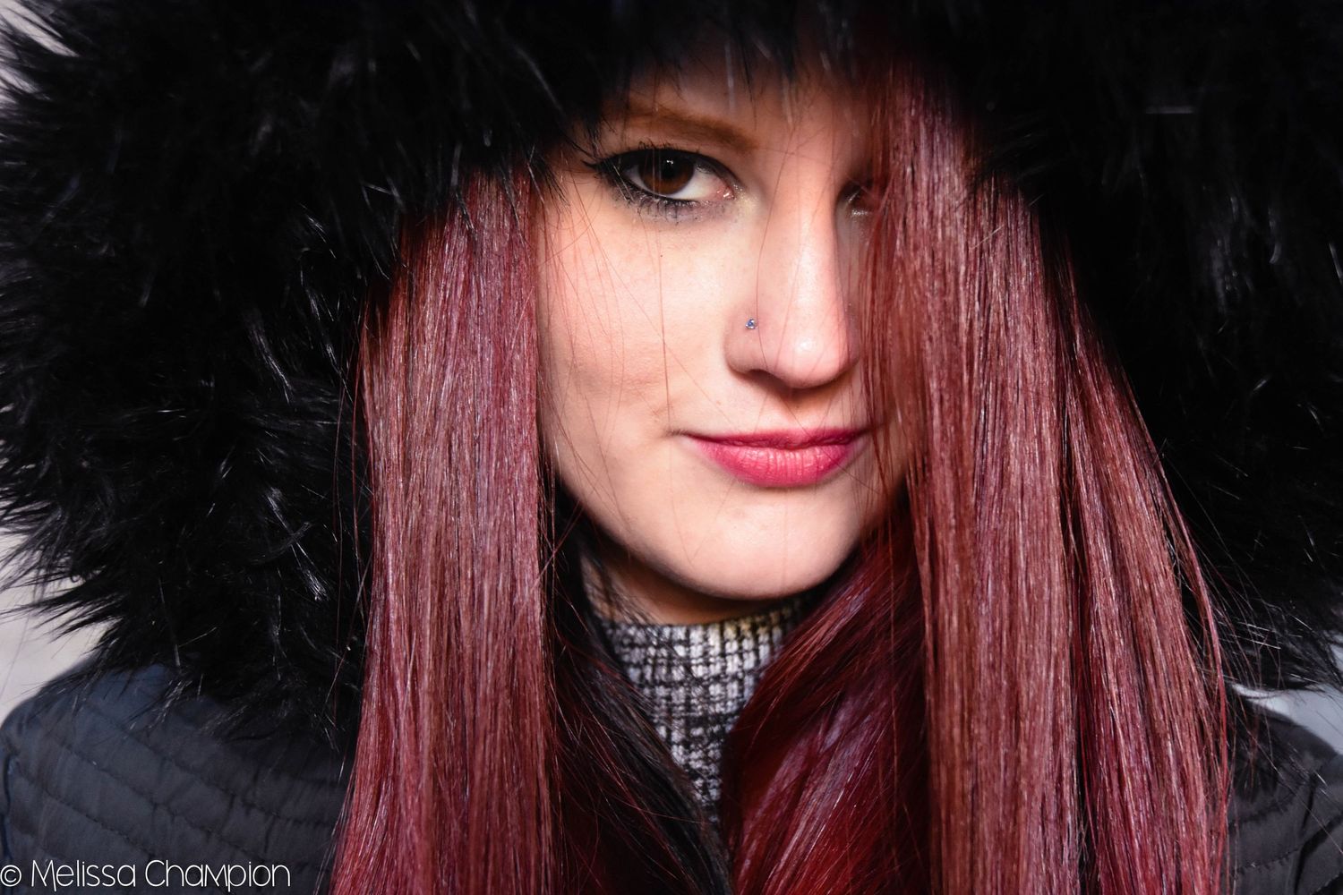 Young woman with red hair wearing a black fur-trimmed hood, close-up portrait photography by Melissa Champion.