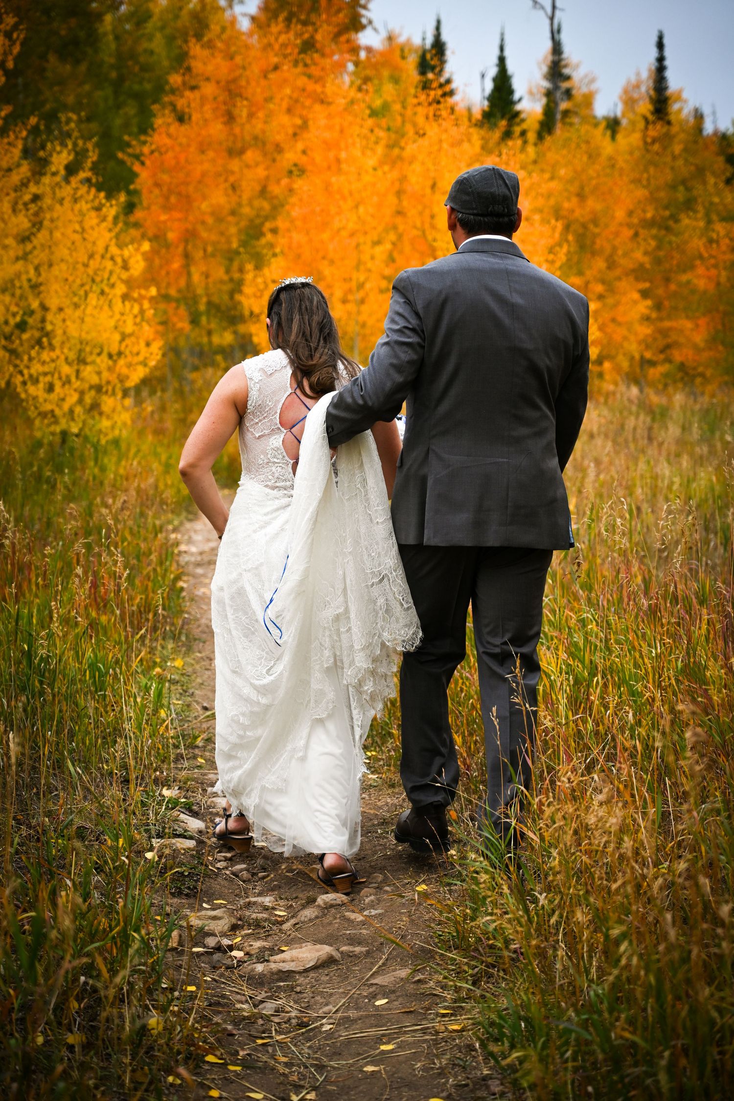 Bride and groom walking hand-in-hand along a path through vibrant autumn aspen trees.