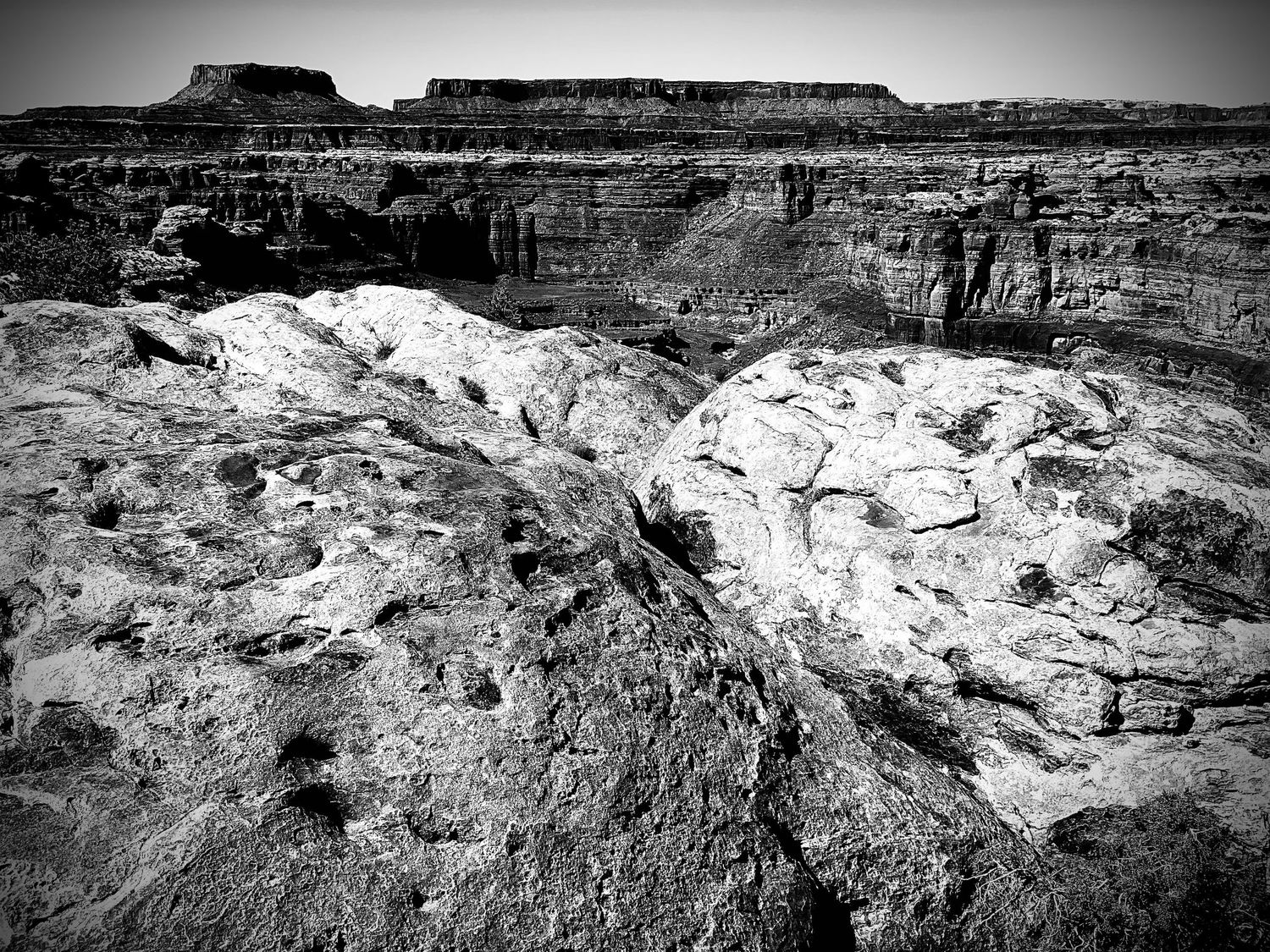 Black and white photo of rugged canyon rock formations with layered cliffs and desert landscape in the background.