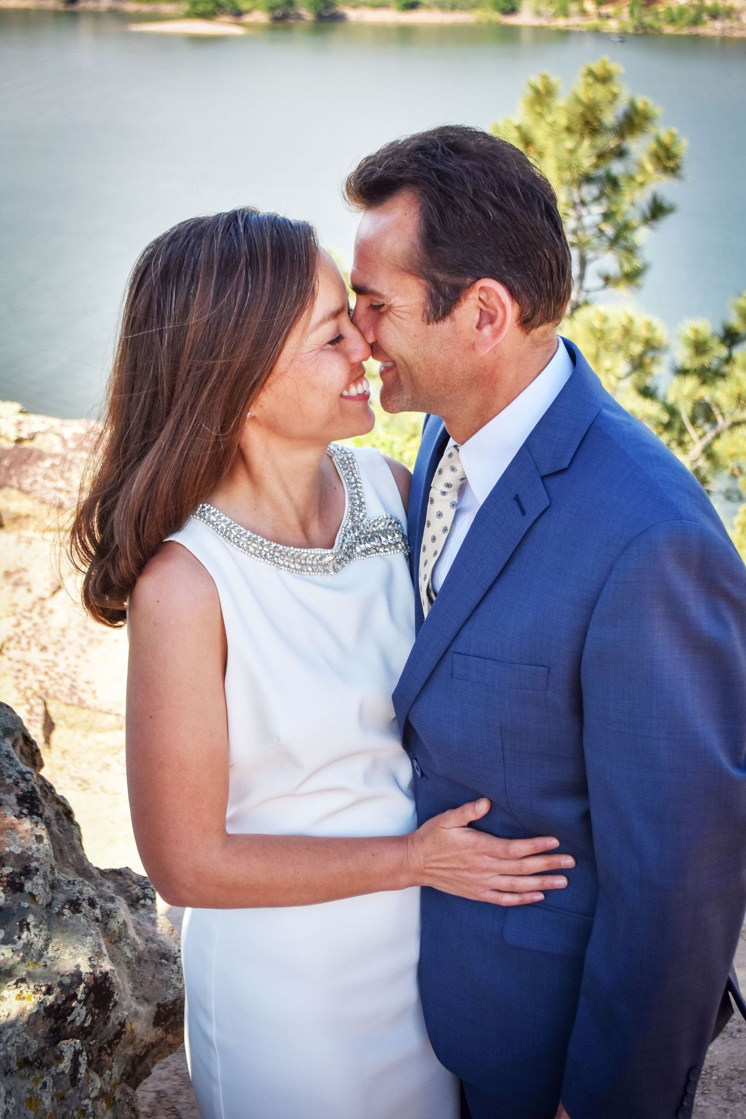 Bride and groom in blue suit sharing an intimate moment near a scenic lake overlook.