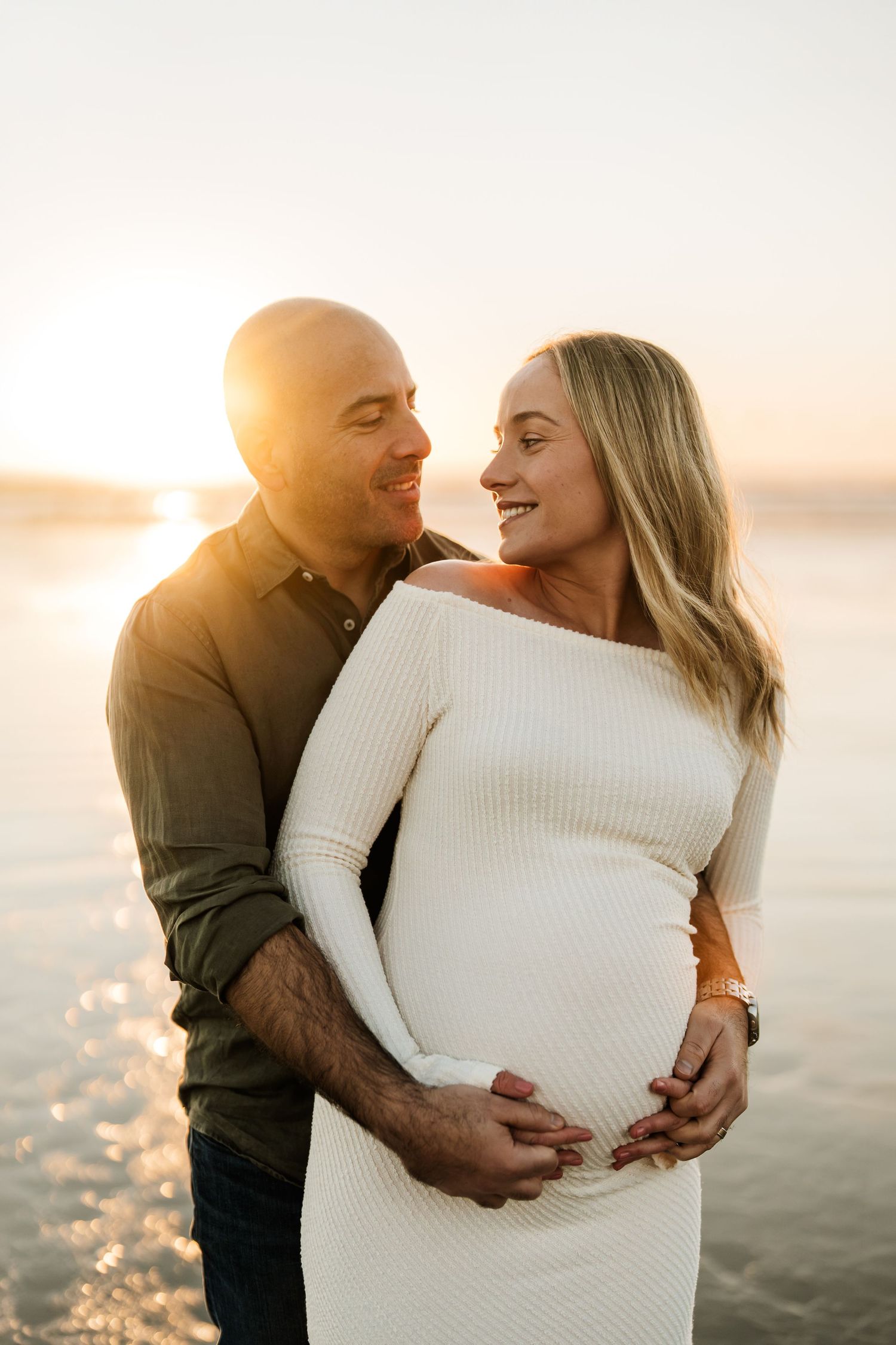 Expecting couple embracing at sunset during a Christchurch beach maternity photography session