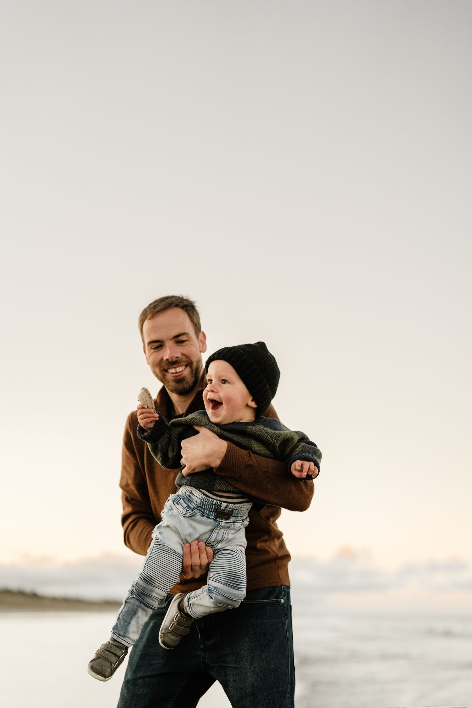 Dad laughing and playing with his young son during a natural family photo session at a Christchurch beach