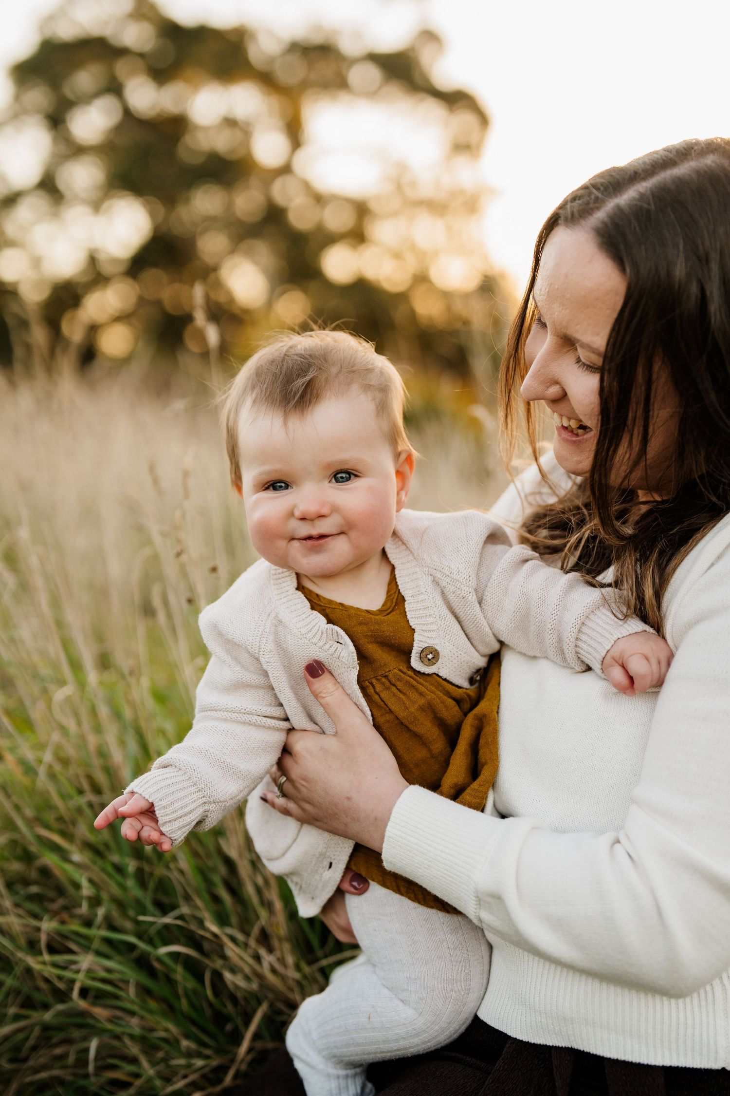 Mum cuddling her baby in long grass during a golden hour family photo session in Christchurch