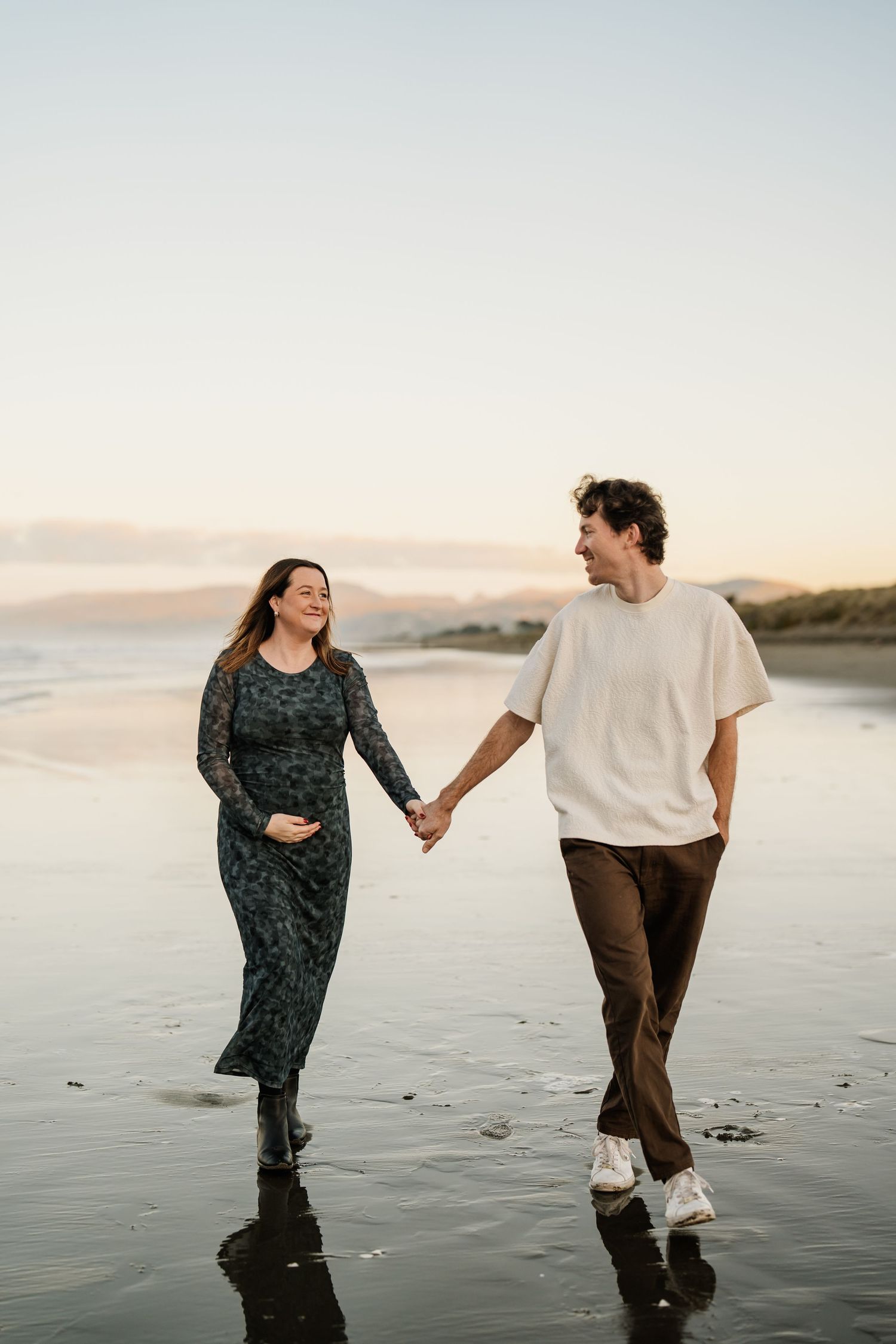 Expecting couple walking hand in hand along a Christchurch beach during a sunset maternity photography session