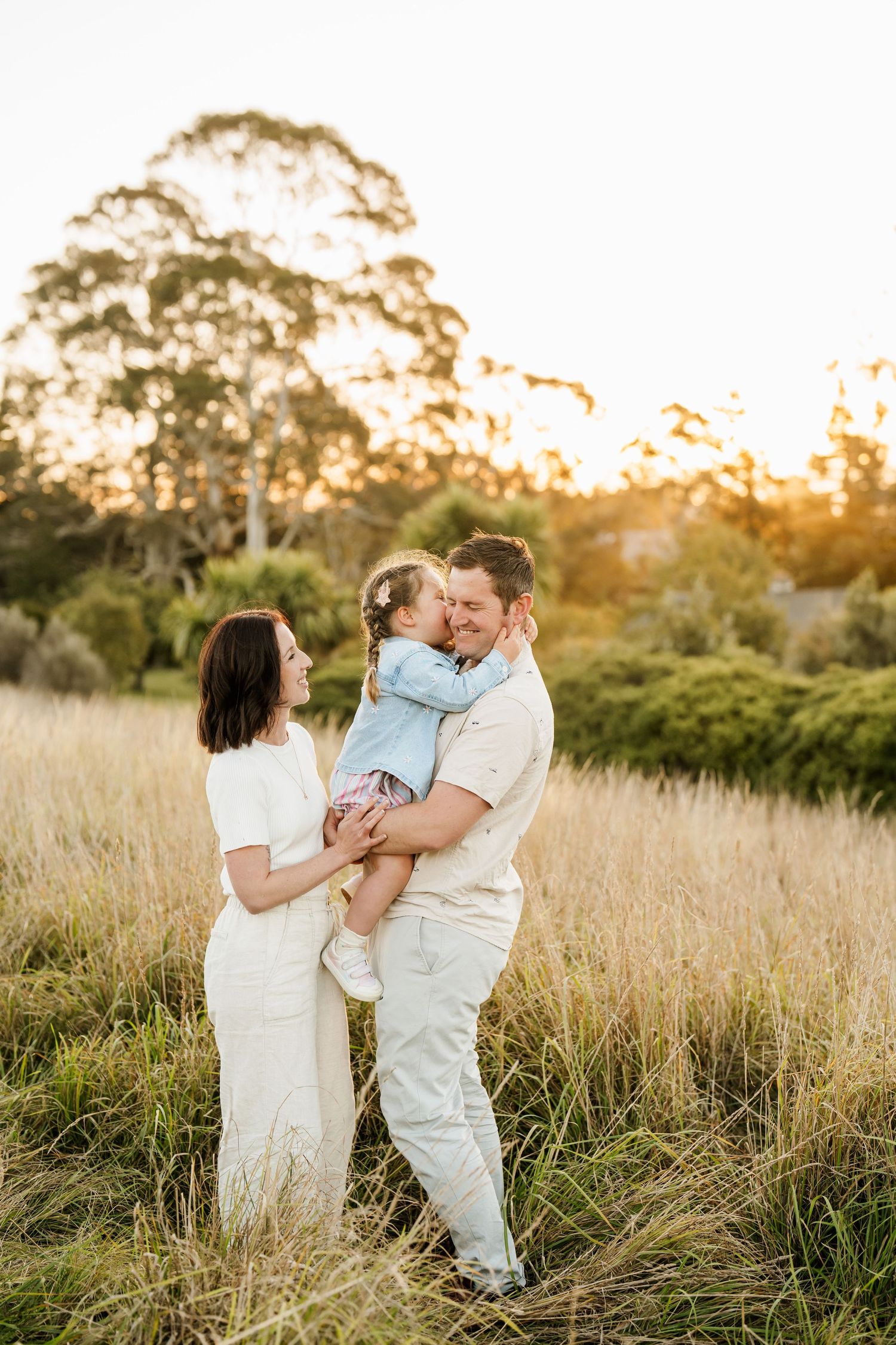 Parents cuddling their young child outdoors during a relaxed Christchurch family photography session