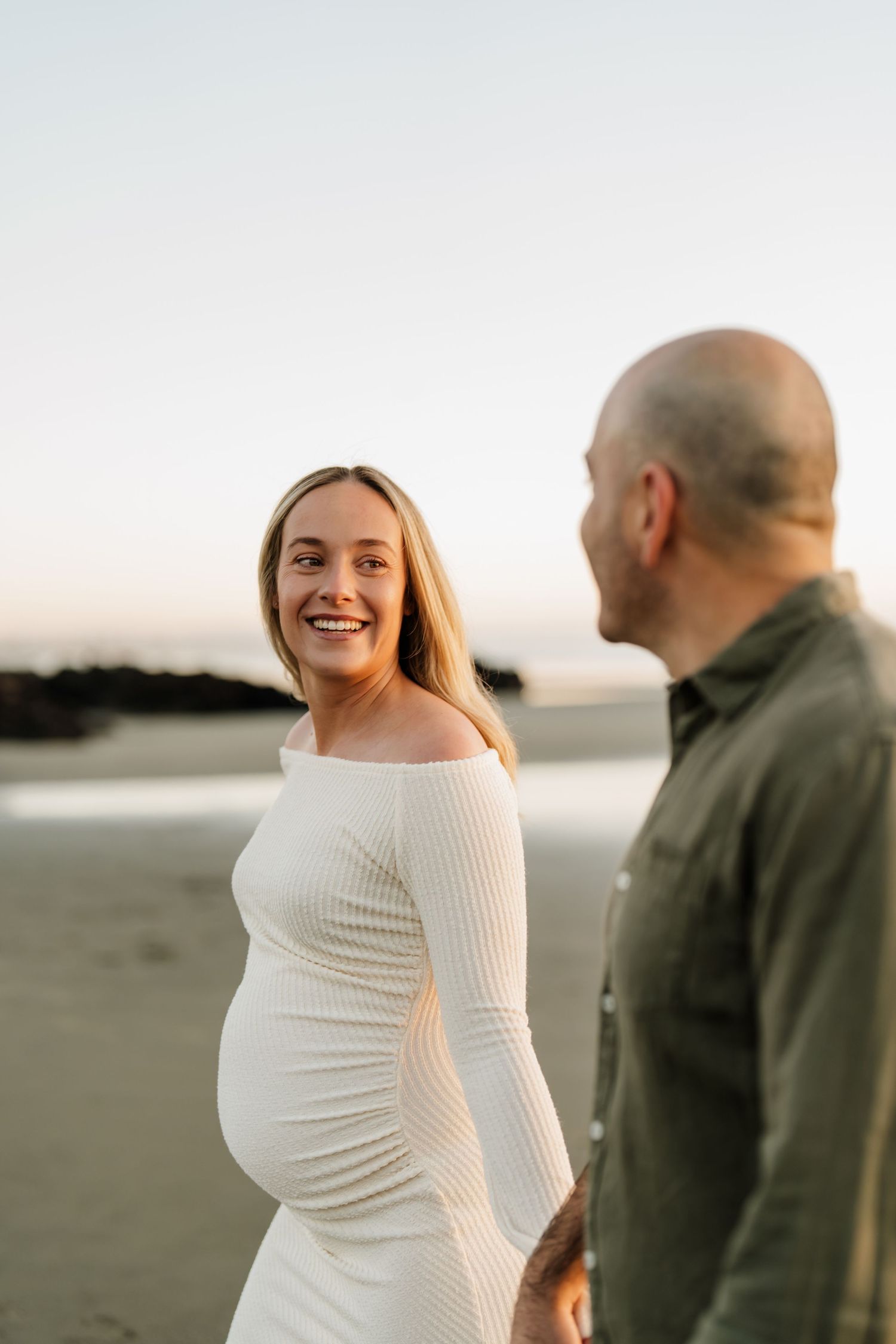 Expectant parents laughing together during their relaxed maternity photography session at Sumner Beach.