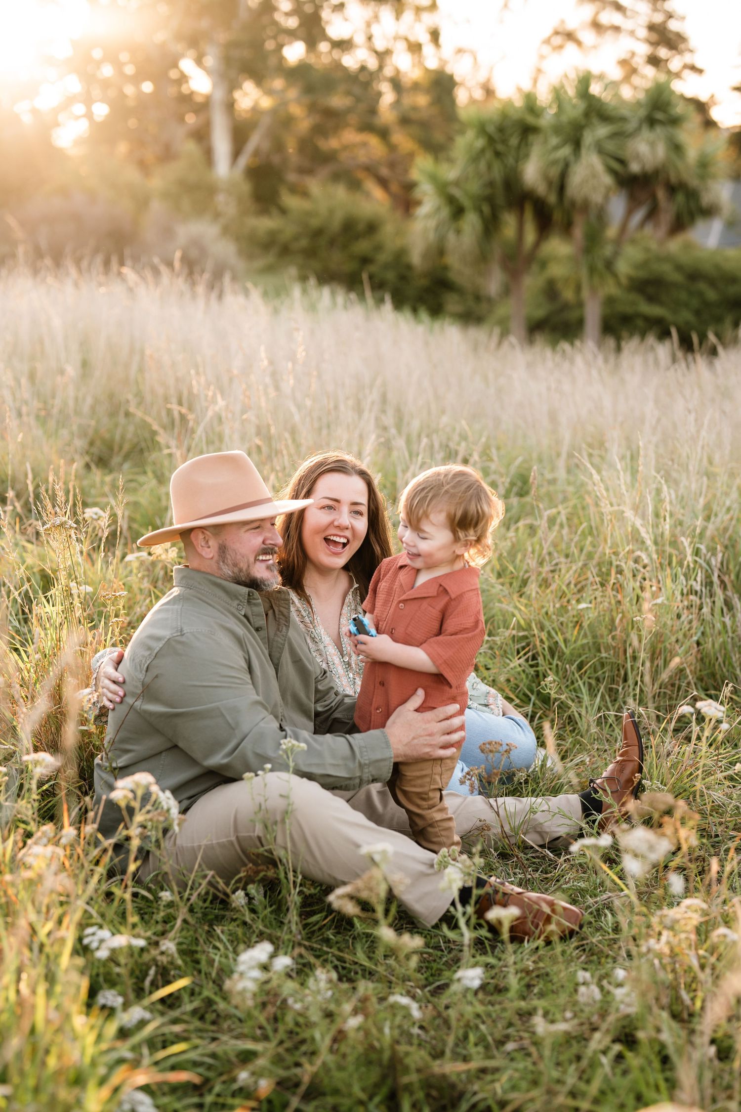 Family sitting together in long grass during a golden hour family photography session in Christchurch