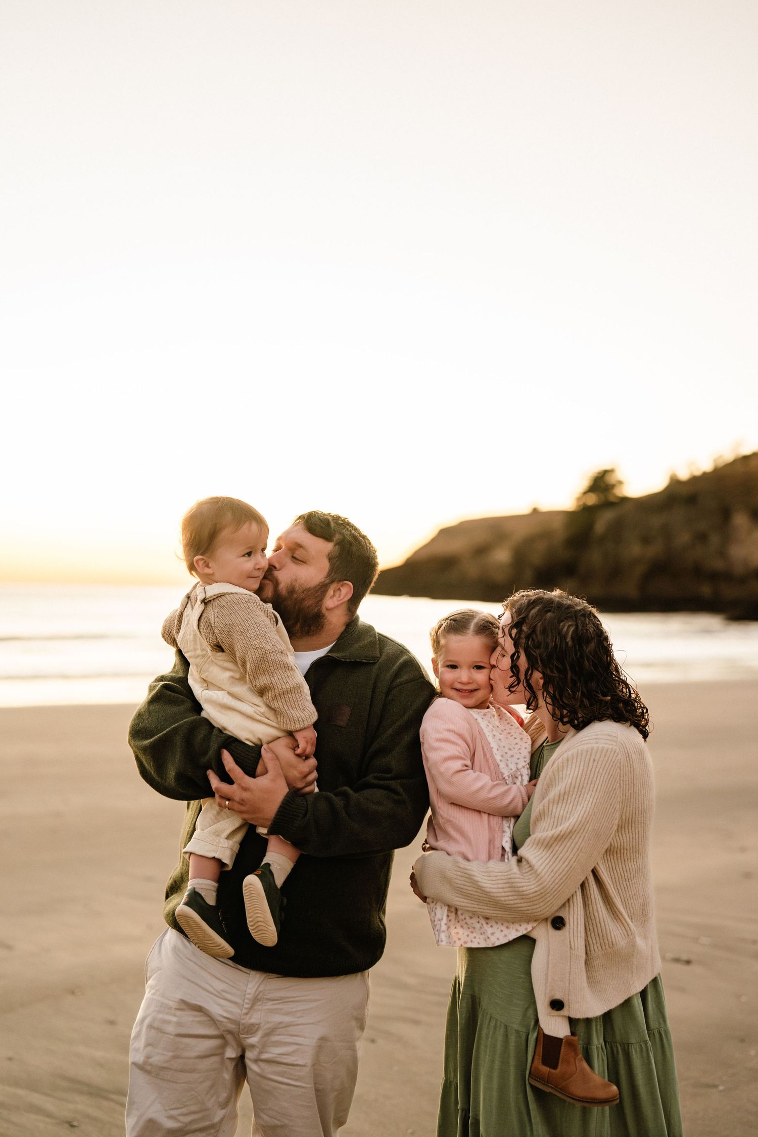 Family of four cuddling and playing together during a sunrise beach photography session in Christchurch