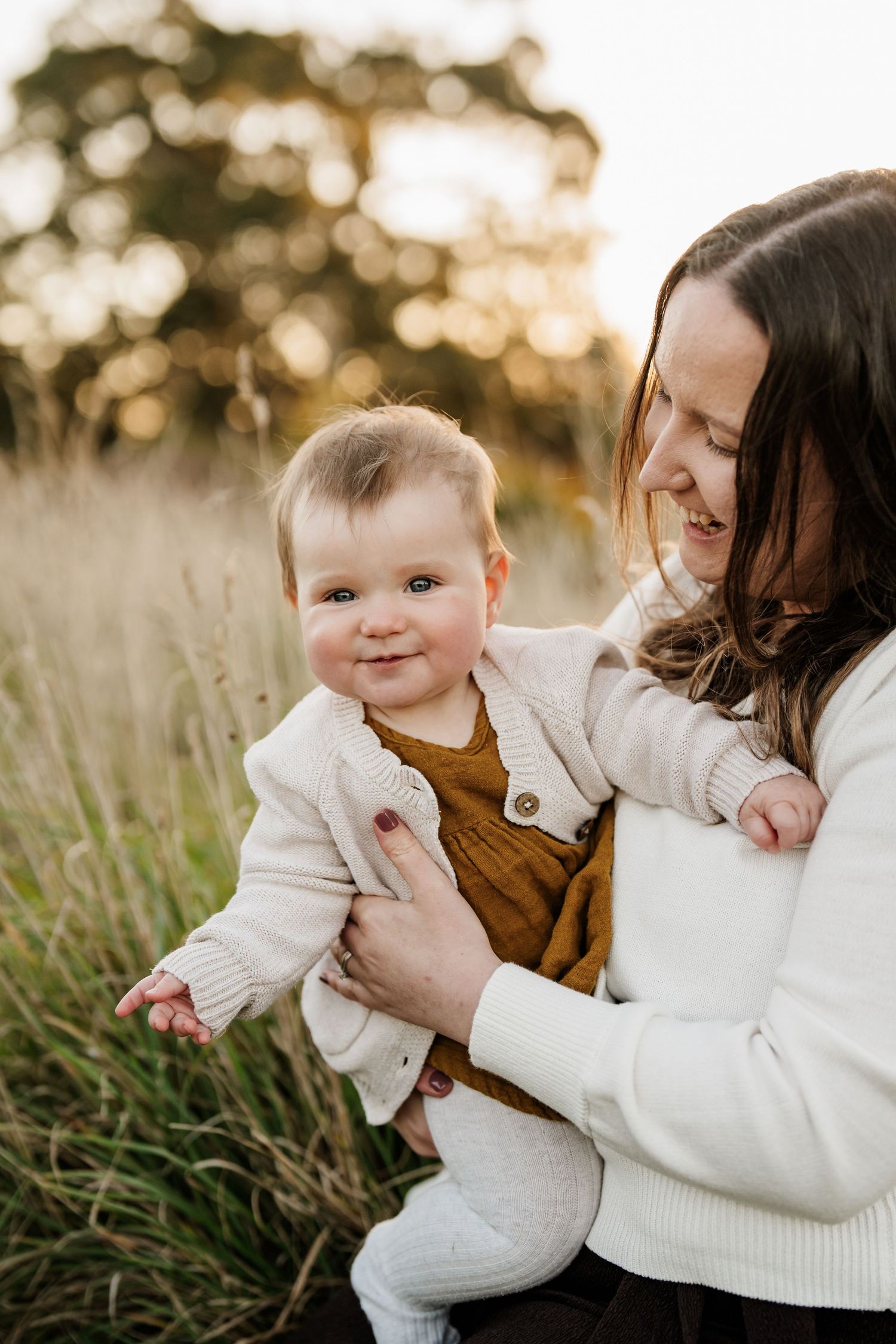 Mum cuddling her baby in long grass during an outdoor family photography session in Christchurch