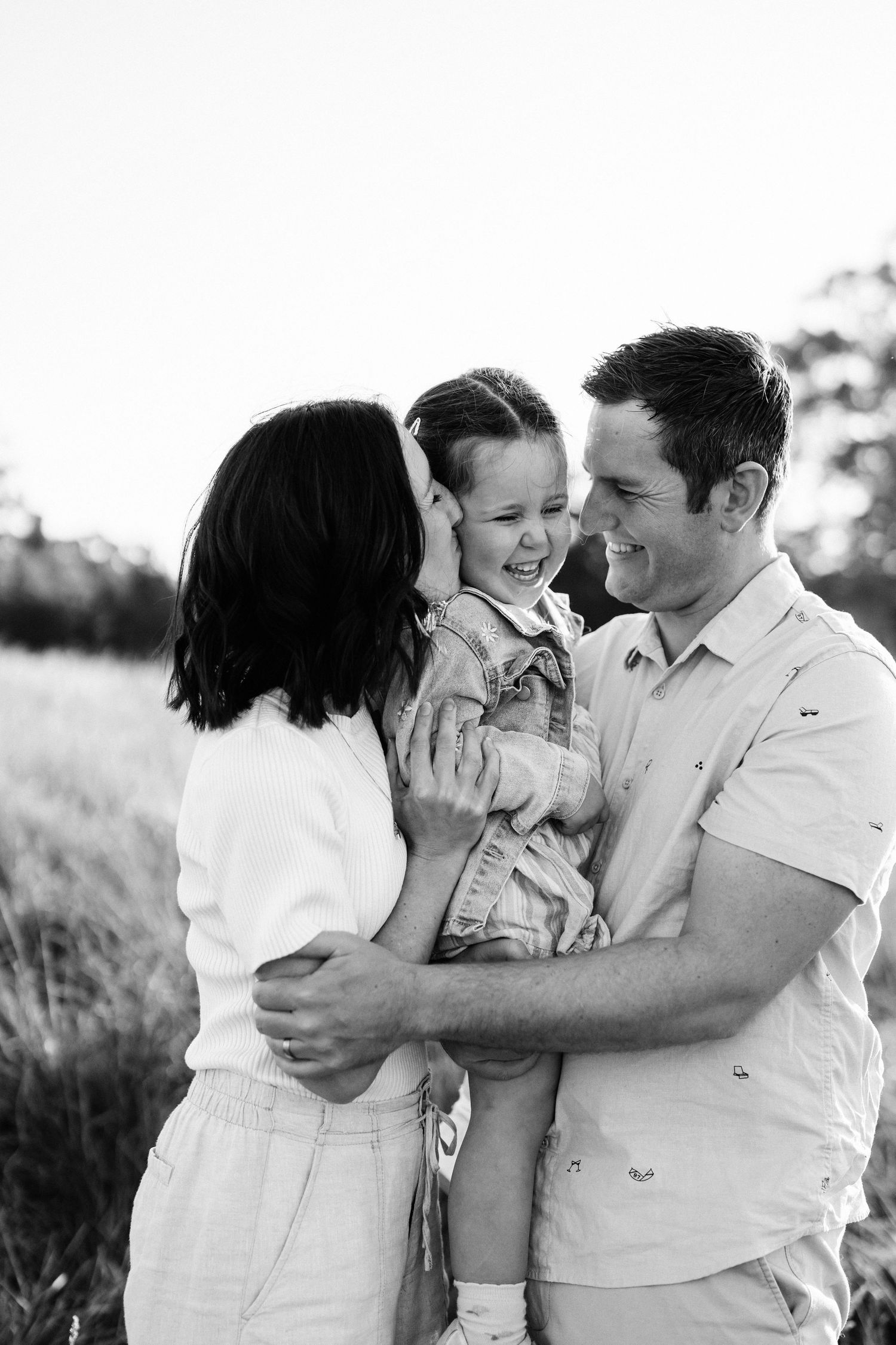 Black and white photo of parents cuddling their young daughter during a relaxed family photography session in Christchurch