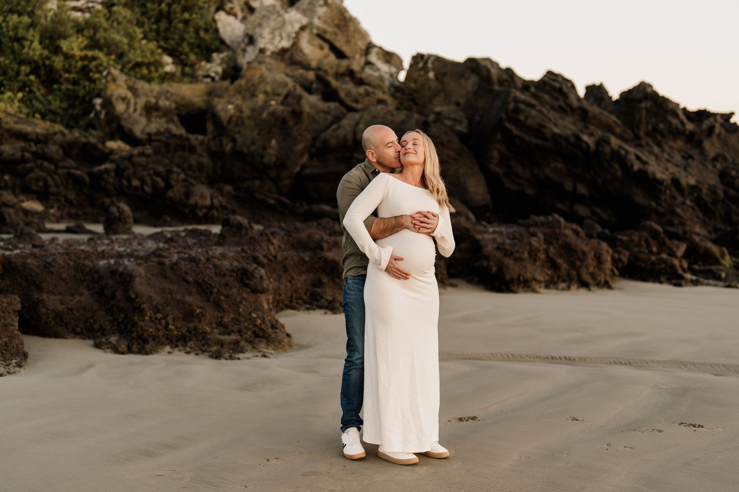 Expectant parents cuddling together during their relaxed beach maternity photography session in Christchurch.