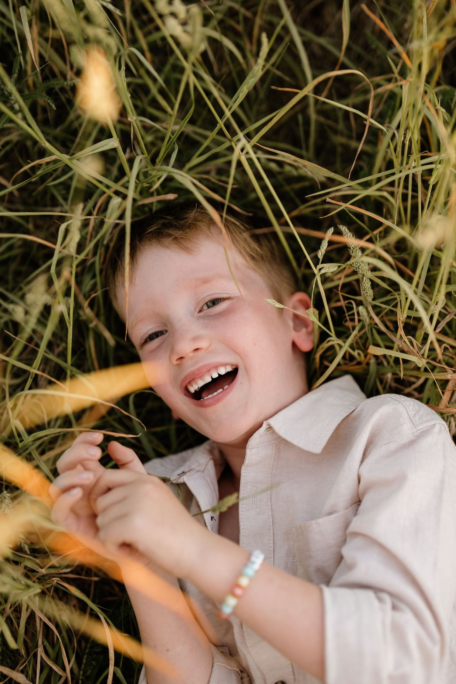 Young boy laughing in long grass during a relaxed outdoor family photography session in Christchurch