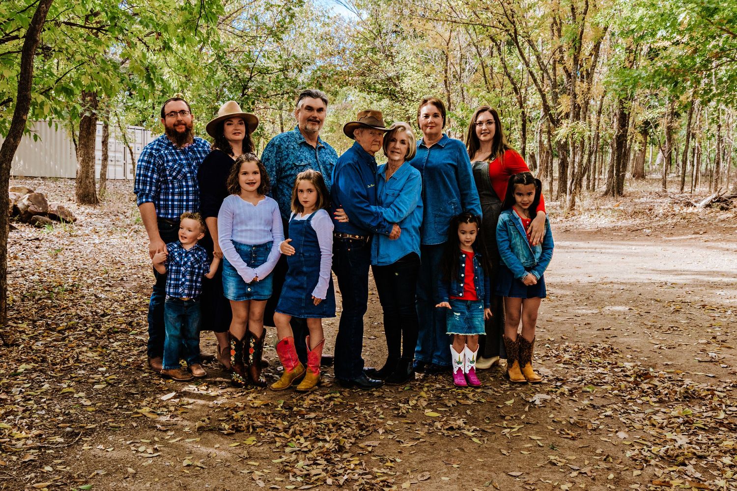 Large family group posing outdoors in wooded area, wearing casual western attire including cowboy hats and denim.
