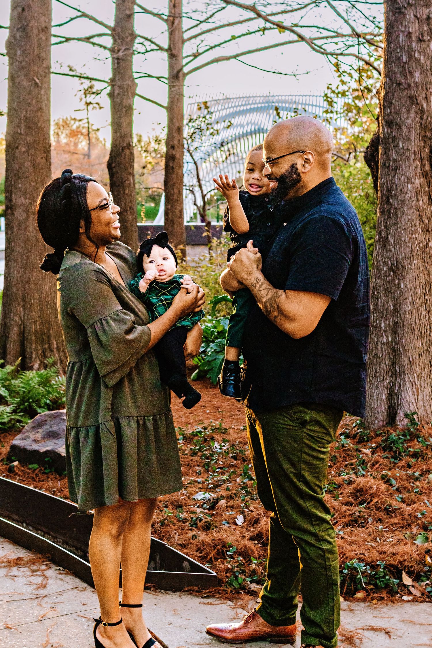A couple shares a romantic moment dancing together among tall trees and fallen autumn leaves in a park setting.