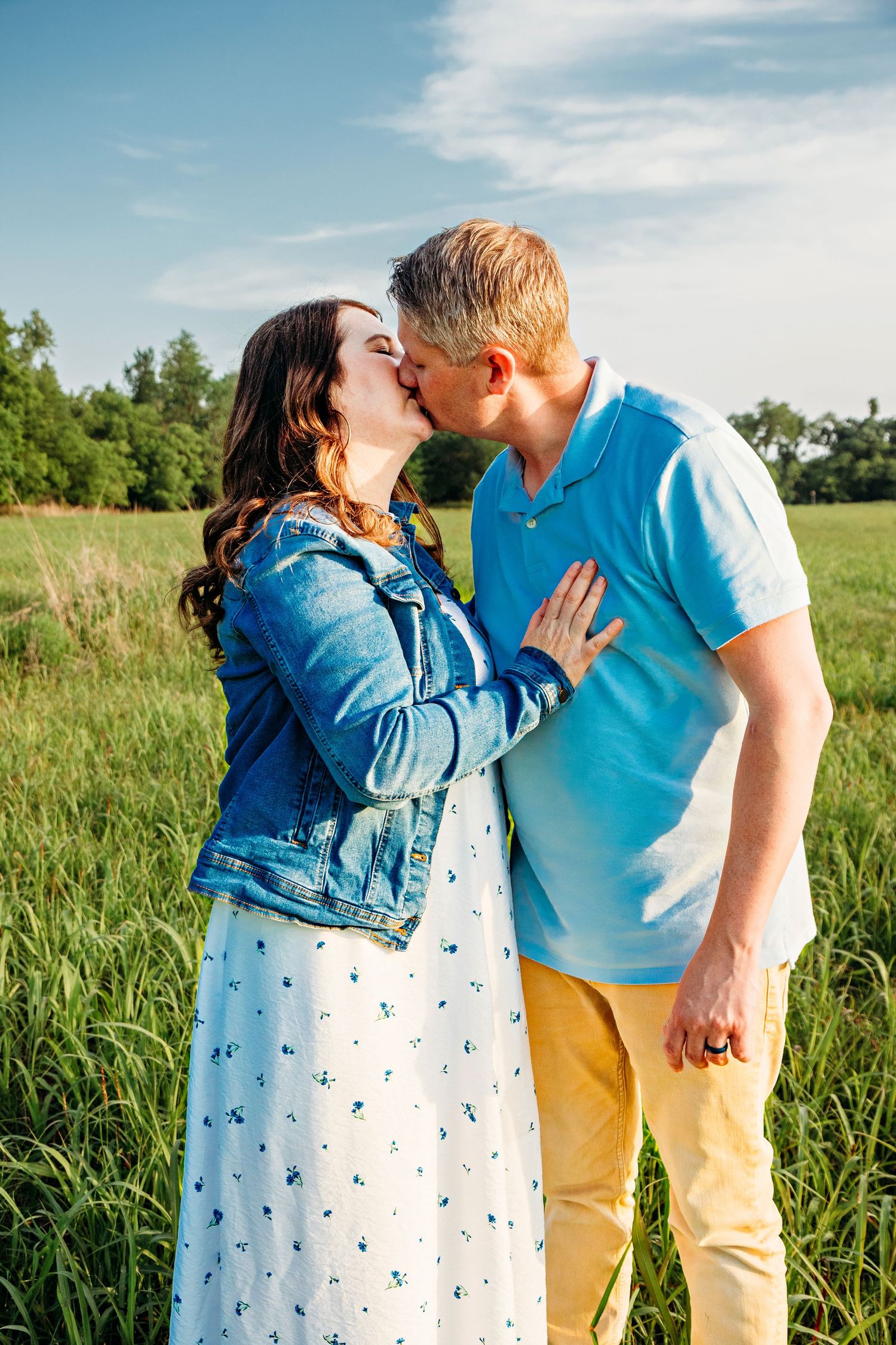 A couple shares a tender moment together in a sunlit grassy field wearing coordinating blue and yellow outfits.