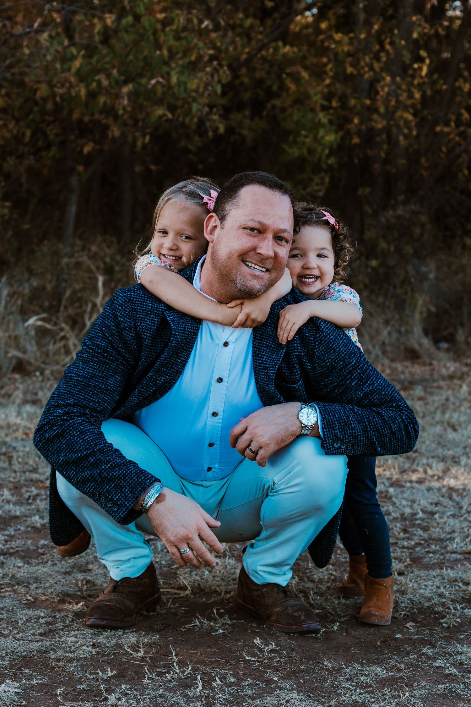 A family wearing coordinated blue outfits poses together crouching on the ground in an outdoor setting.