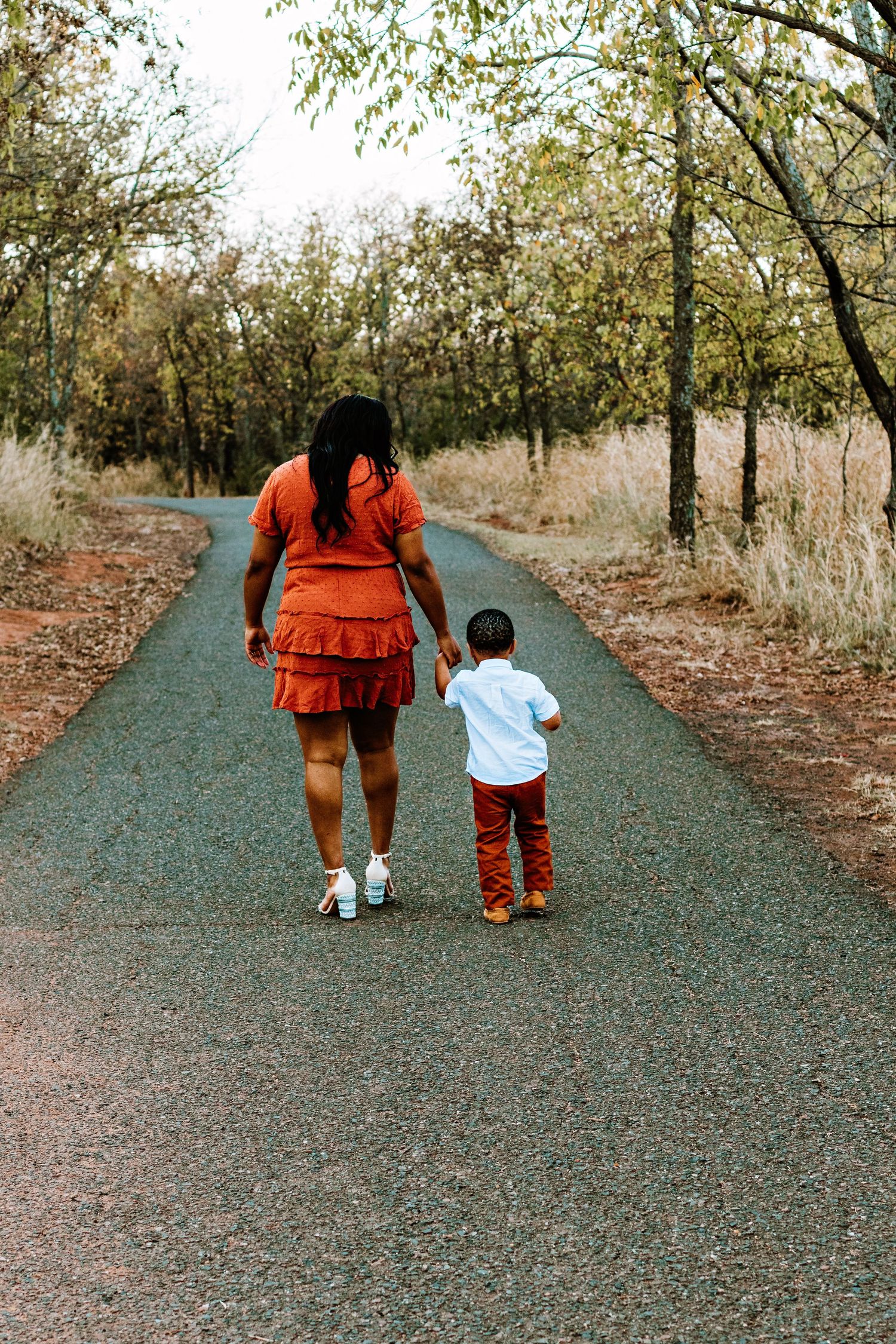 Two people walking together down a tree-lined gravel path in matching rust-colored outfits.