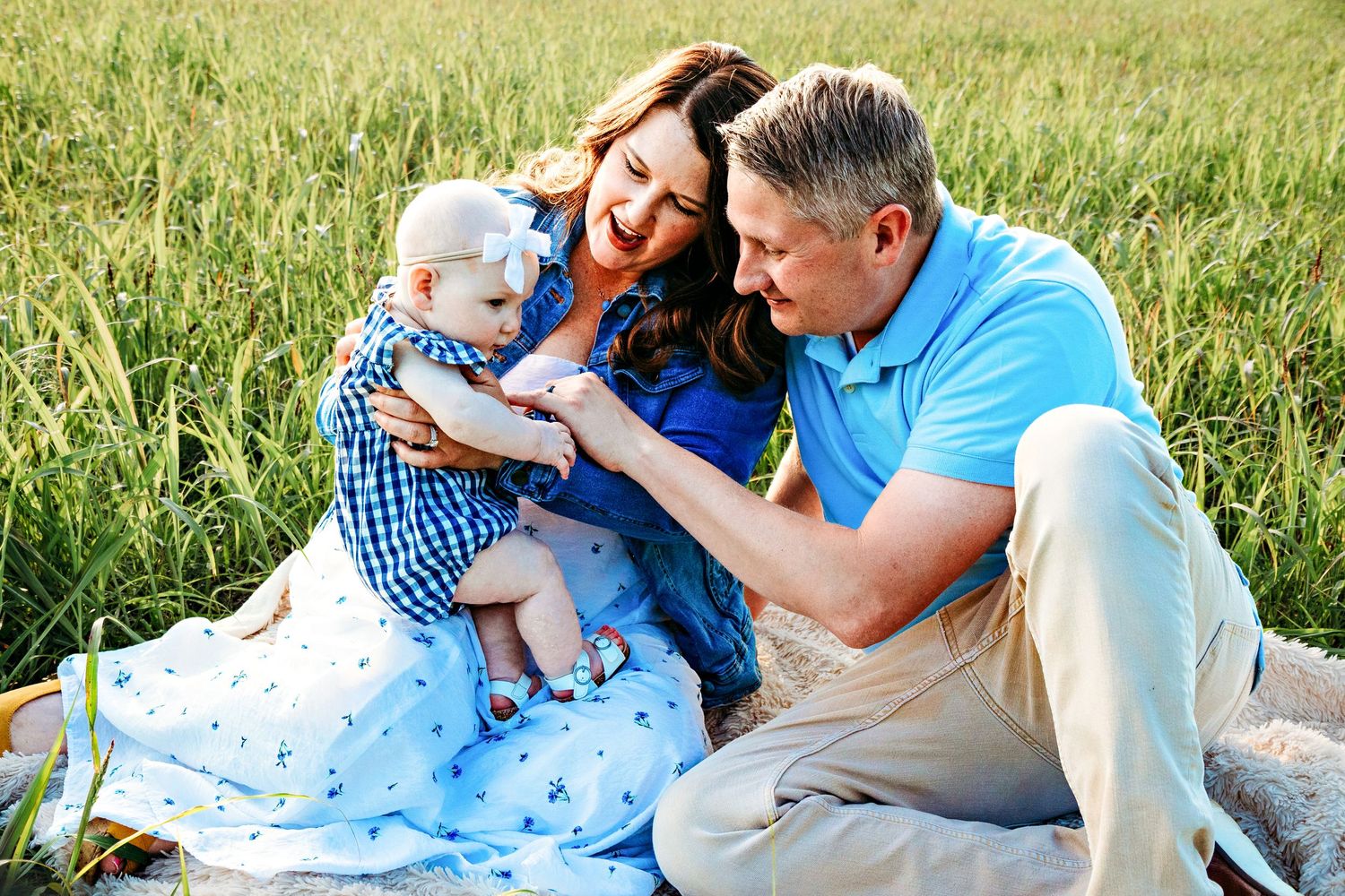 Family enjoying a tender moment together while relaxing on a blanket in a sunny meadow.