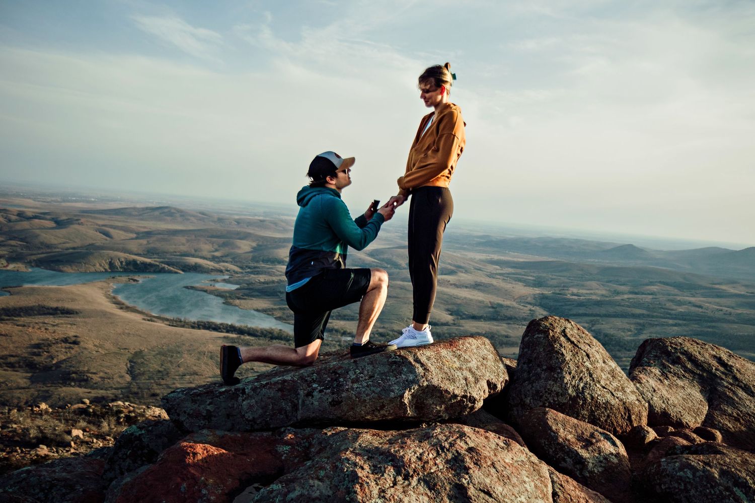 A romantic proposal unfolds on a scenic mountaintop overlook with dramatic views of rolling hills and valleys below.