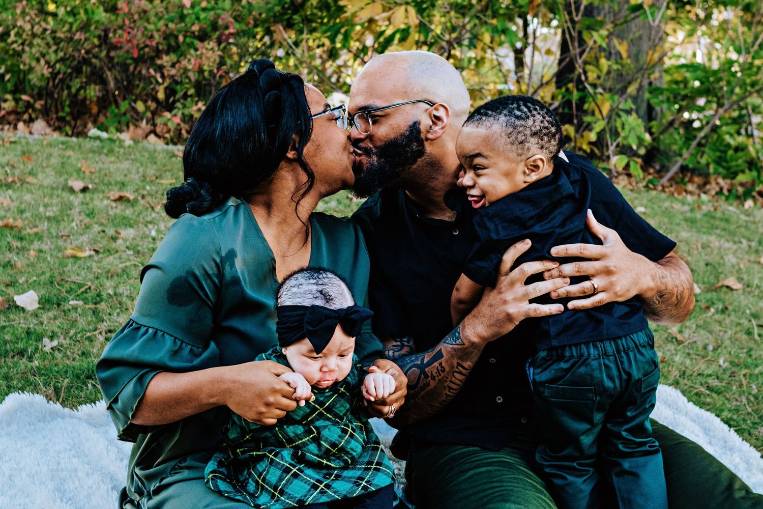 A family shares a joyful moment together while sitting on a blanket outdoors in a garden setting.