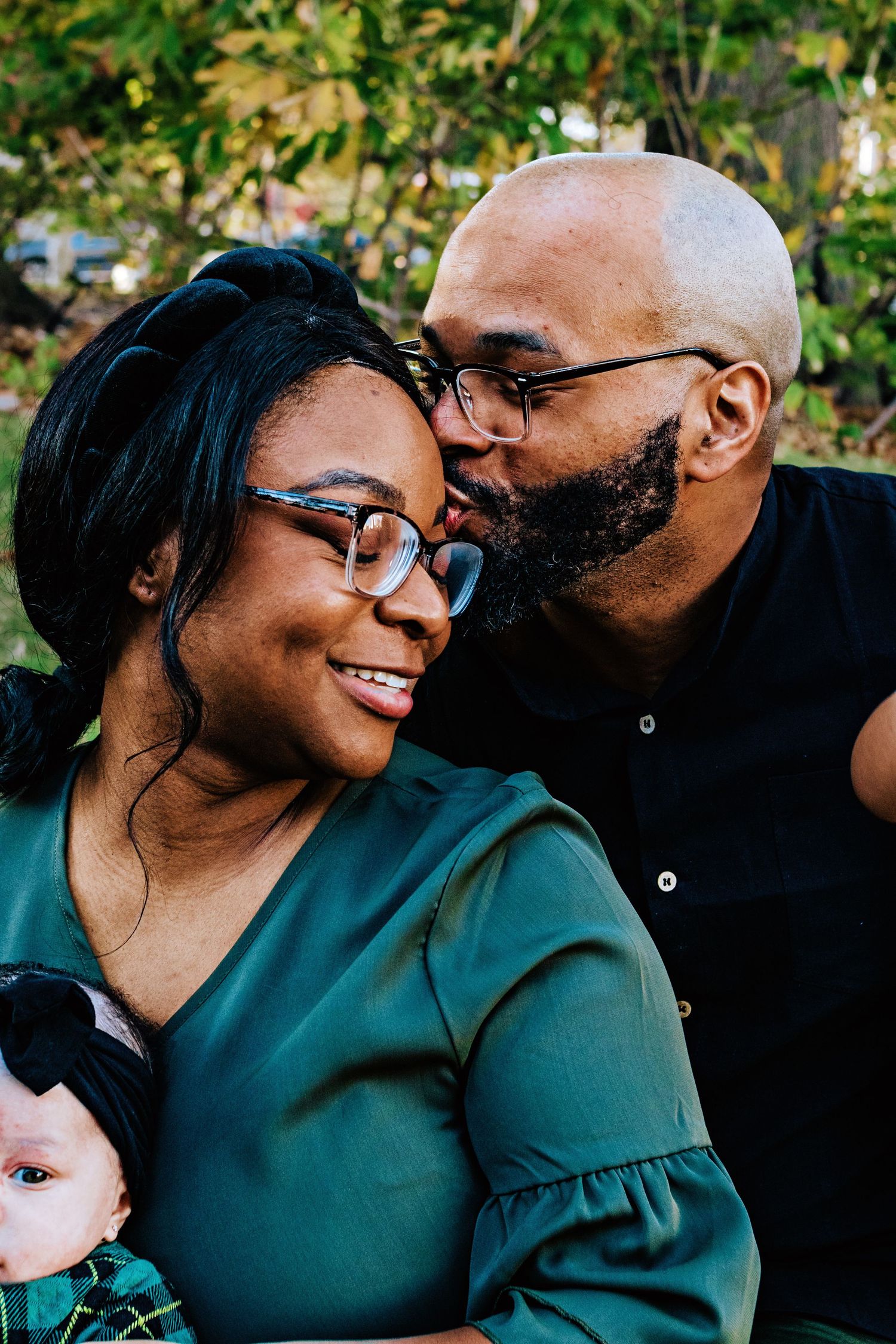 A loving couple shares tender moments outdoors while wearing green and black clothing.