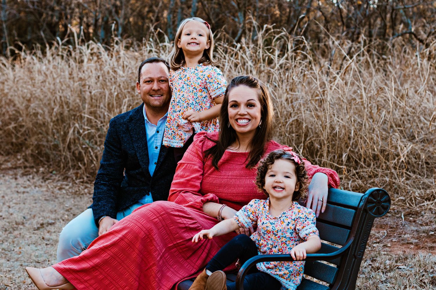 A family wearing red and blue outfits poses together outdoors in a field with dried grass during a photo session.