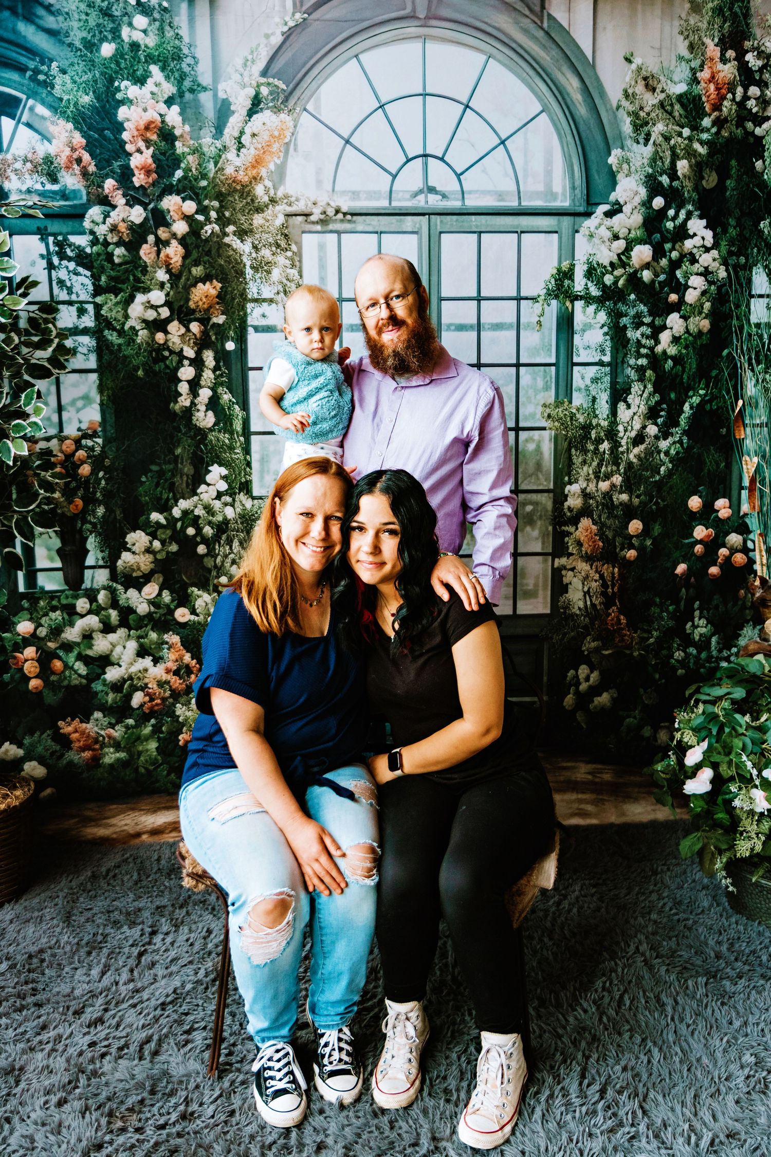 Family portrait session in a greenhouse setting with arched windows and climbing roses creating a romantic backdrop.