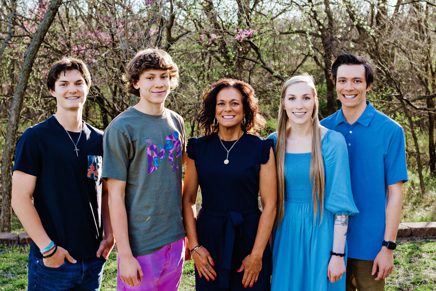 Group of young people standing together outdoors in casual attire against natural background.