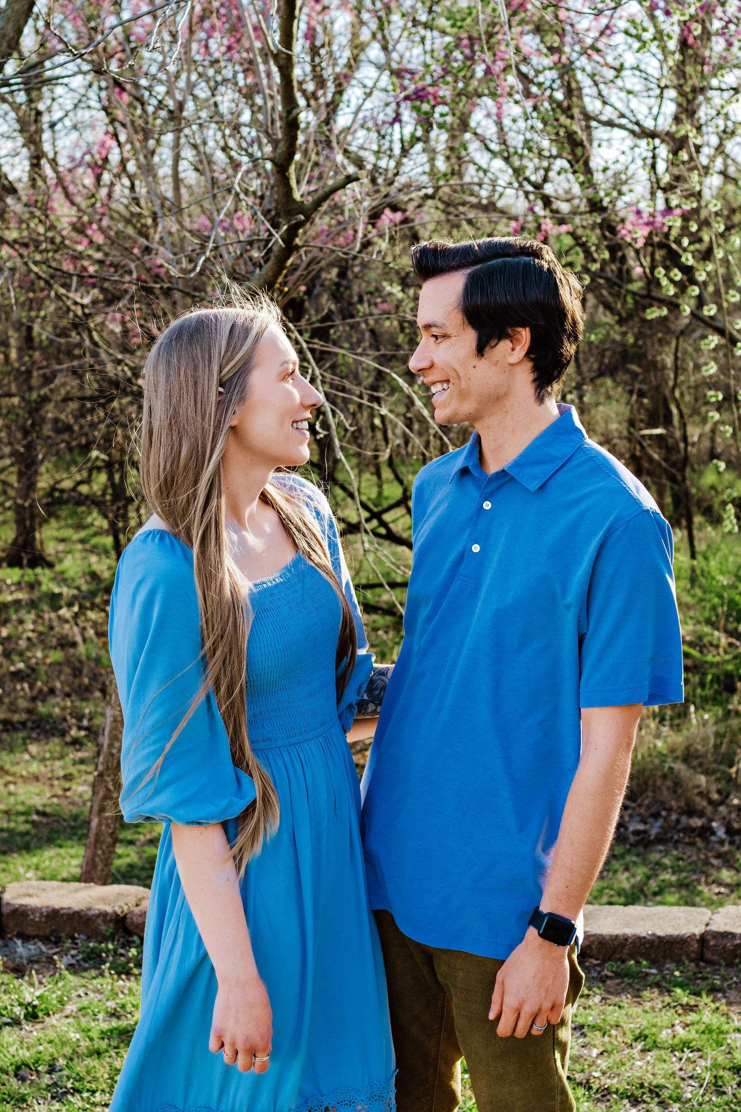Couple in matching blue shirts share loving glances while standing in a blooming spring garden.
