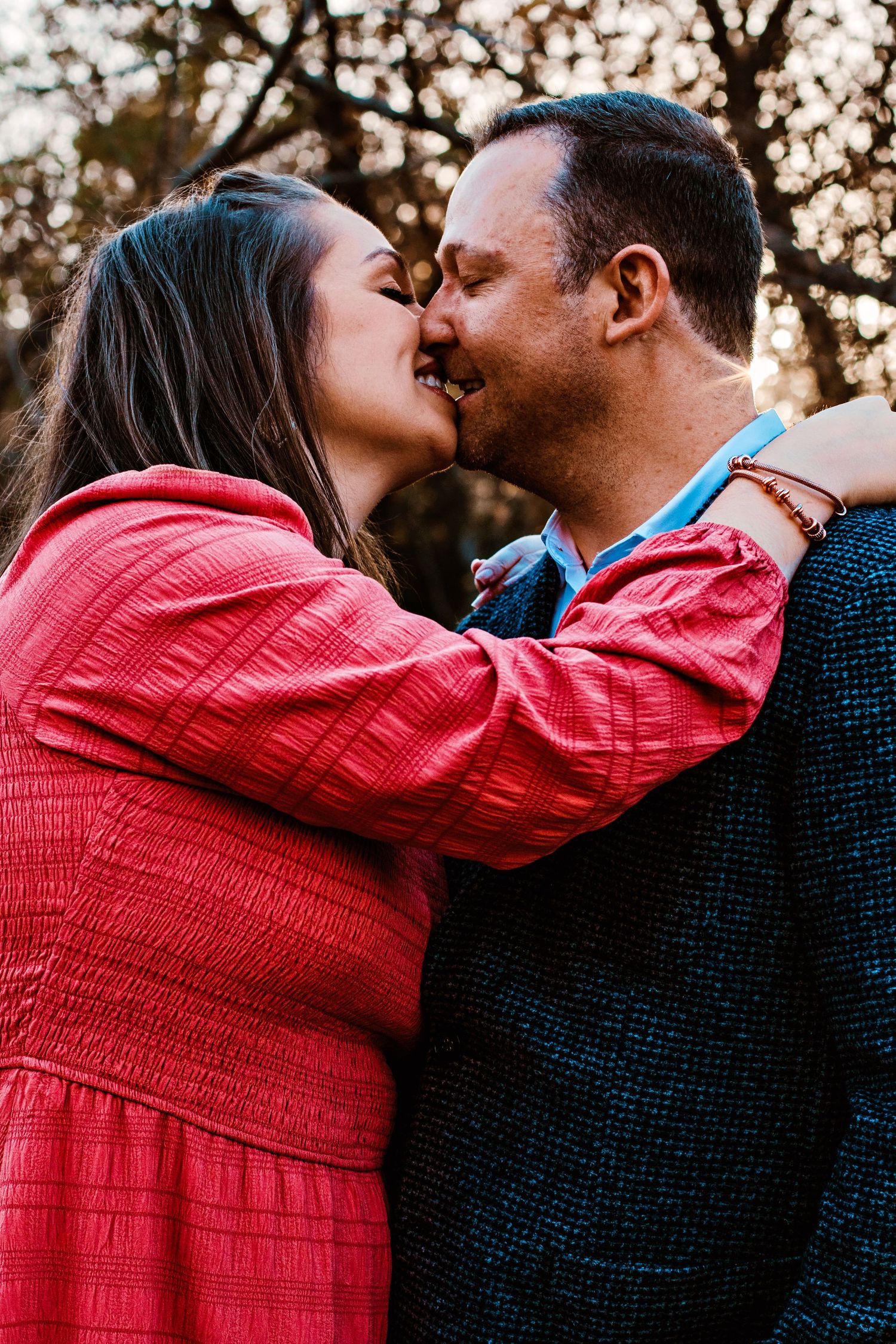 A couple shares a romantic kiss outdoors at sunset wearing red and blue clothing in a series of connected photos.