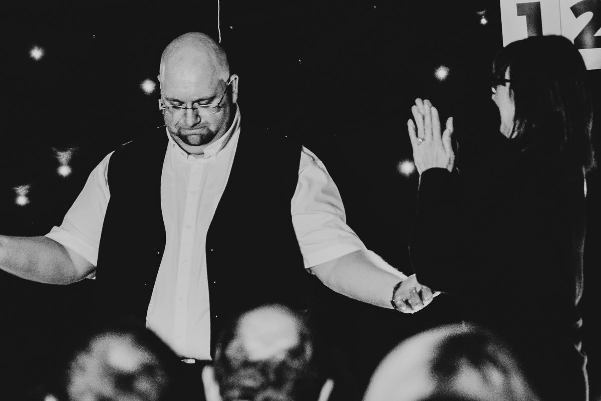 A bald man performing on stage in black and white photography at an indoor event.