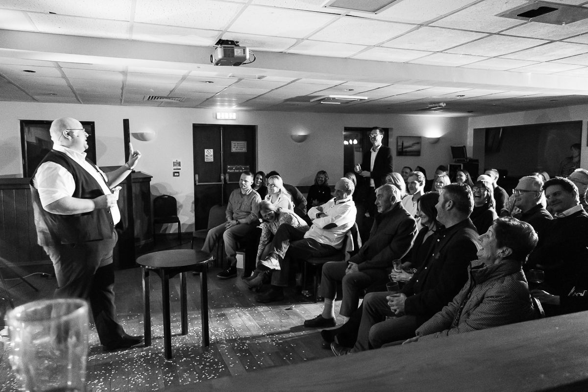 A magician performs for a seated audience in a dimly lit room during a corporate or private event.