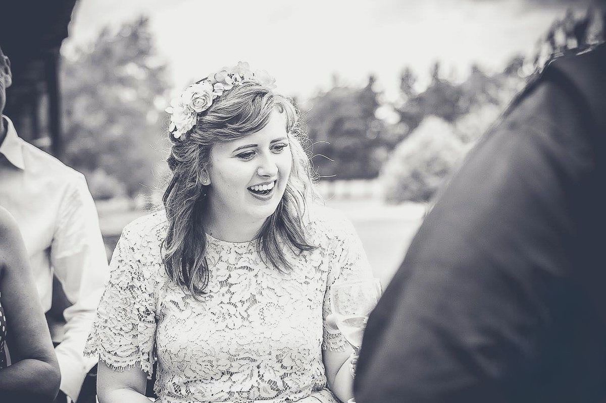 Bride wearing floral crown laughing joyfully at outdoor wedding ceremony in black and white.