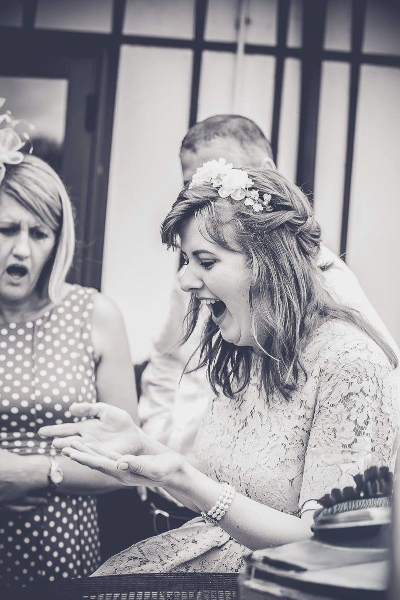 Black and white photo of a bride laughing with flower crown, examining her ring at a wedding celebration.