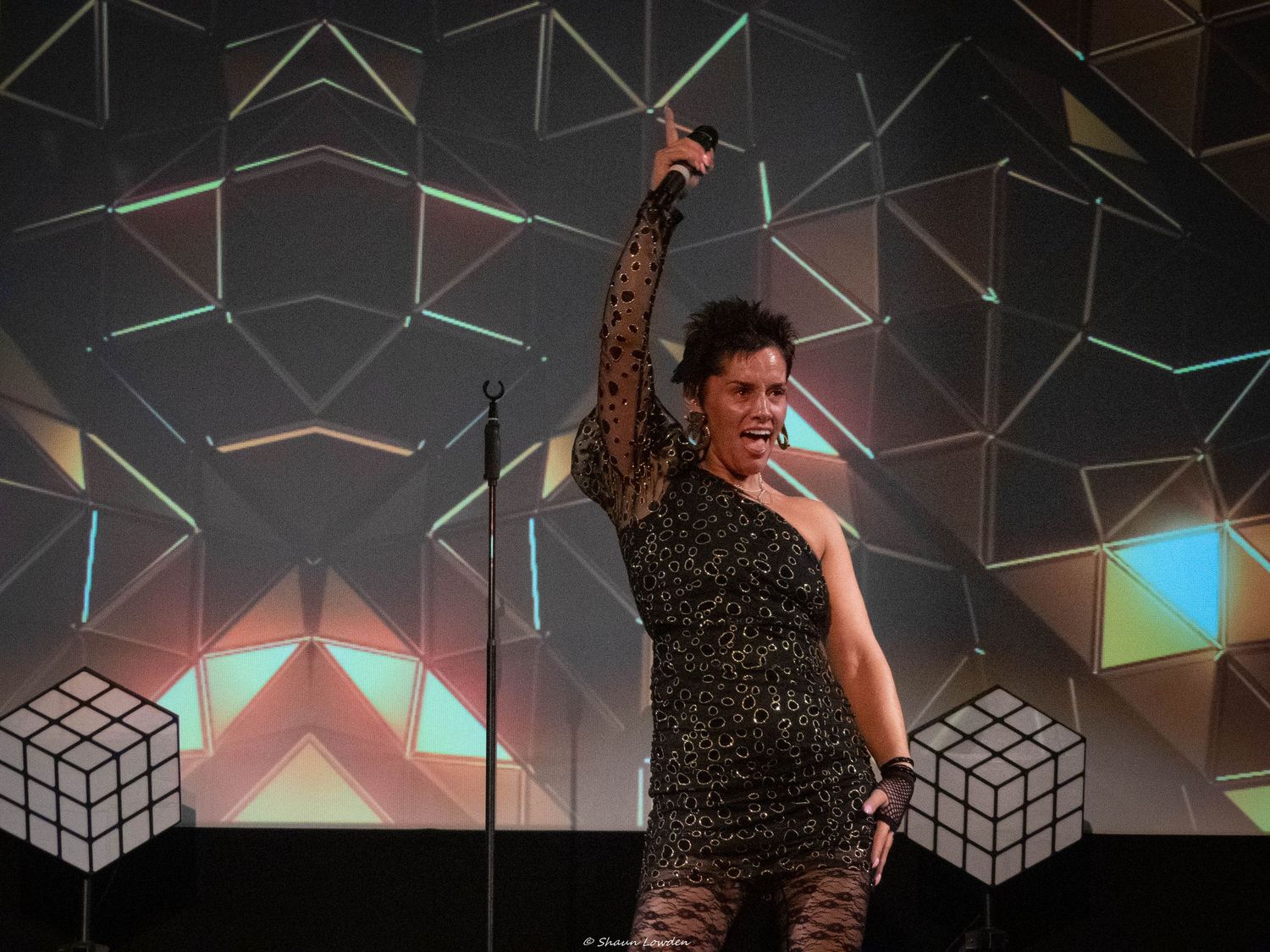 Stage performers against a geometric pattern backdrop with dramatic lighting effects.